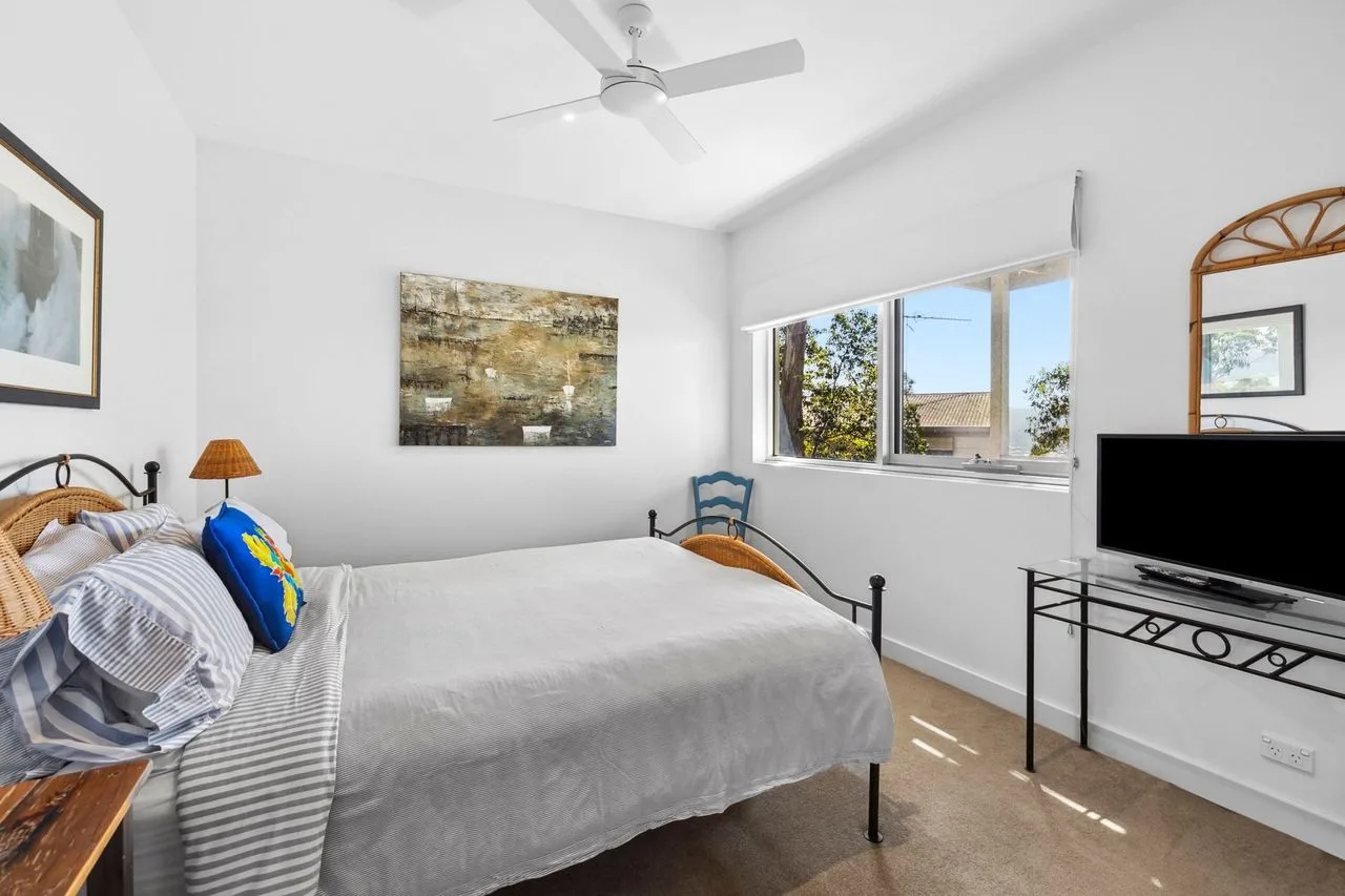 Un dormitorio luminoso con una cama grande y una ventana con vista a los árboles.