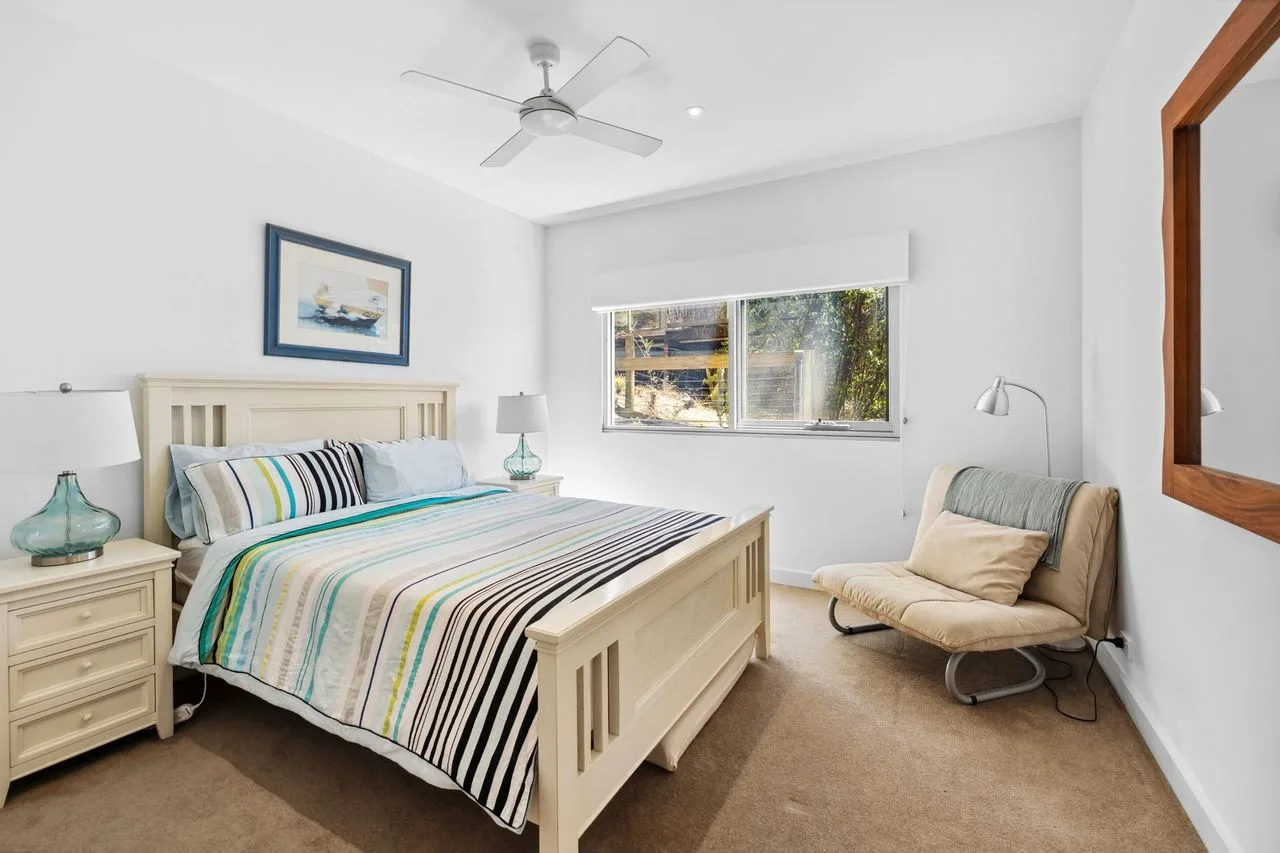 Un dormitorio luminoso con una cama tendida y una silla junto a la ventana.