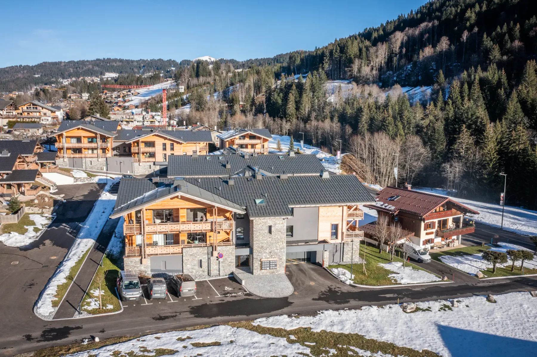 A mountain village with clustered buildings, snow patches, and forested slopes.