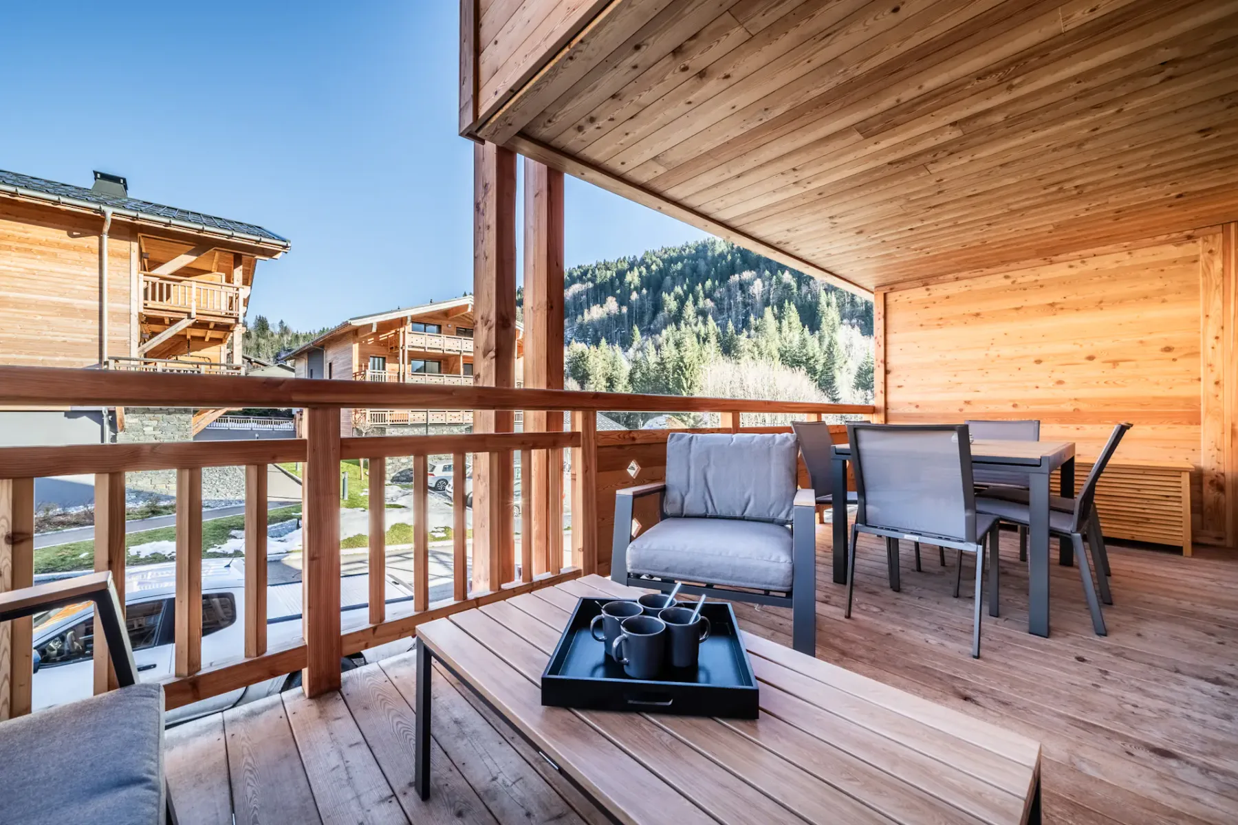 A covered wooden terrace has seating and a dining table overlooking a forested mountain.