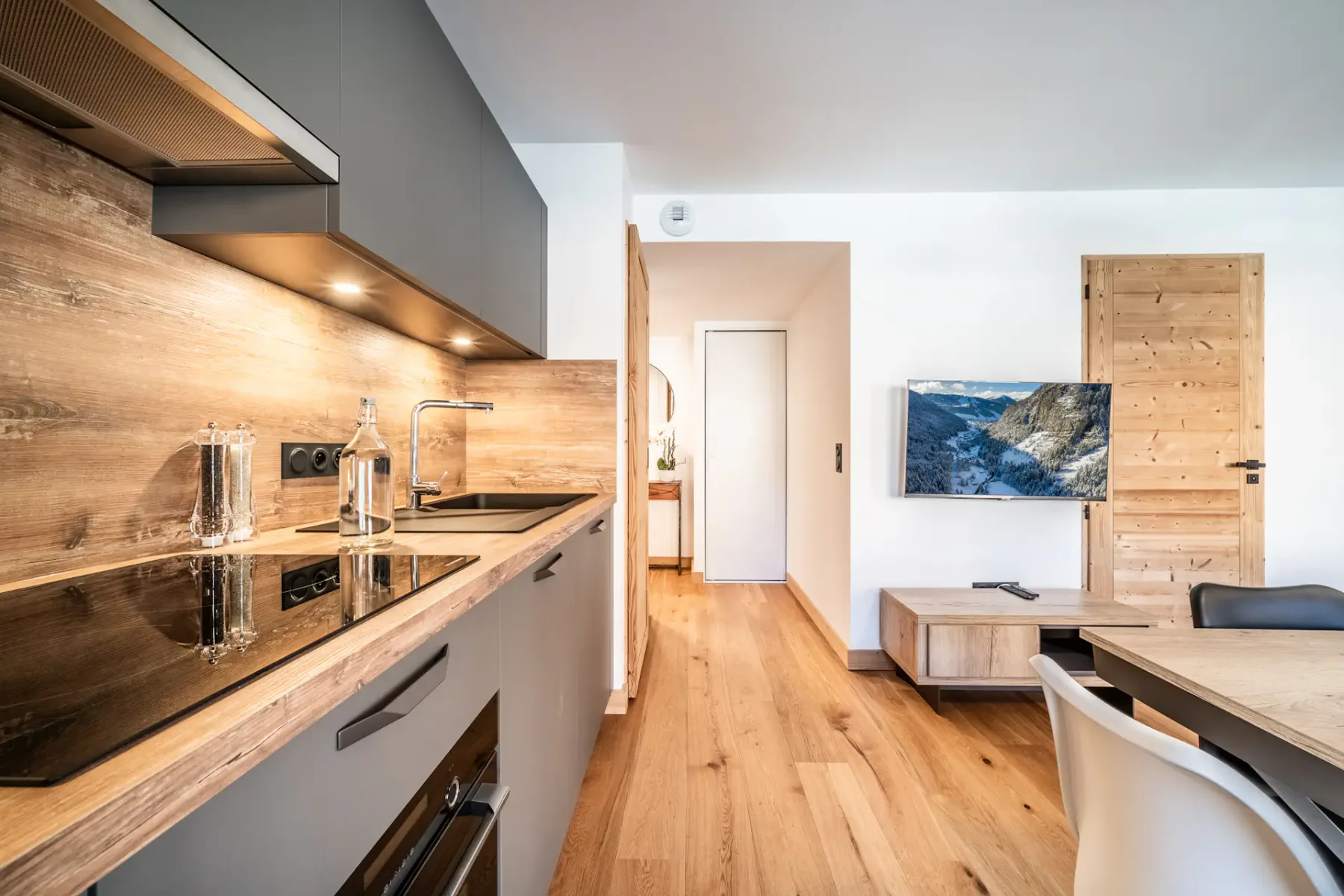 A modern kitchen opens onto a living area with a television and seating.
