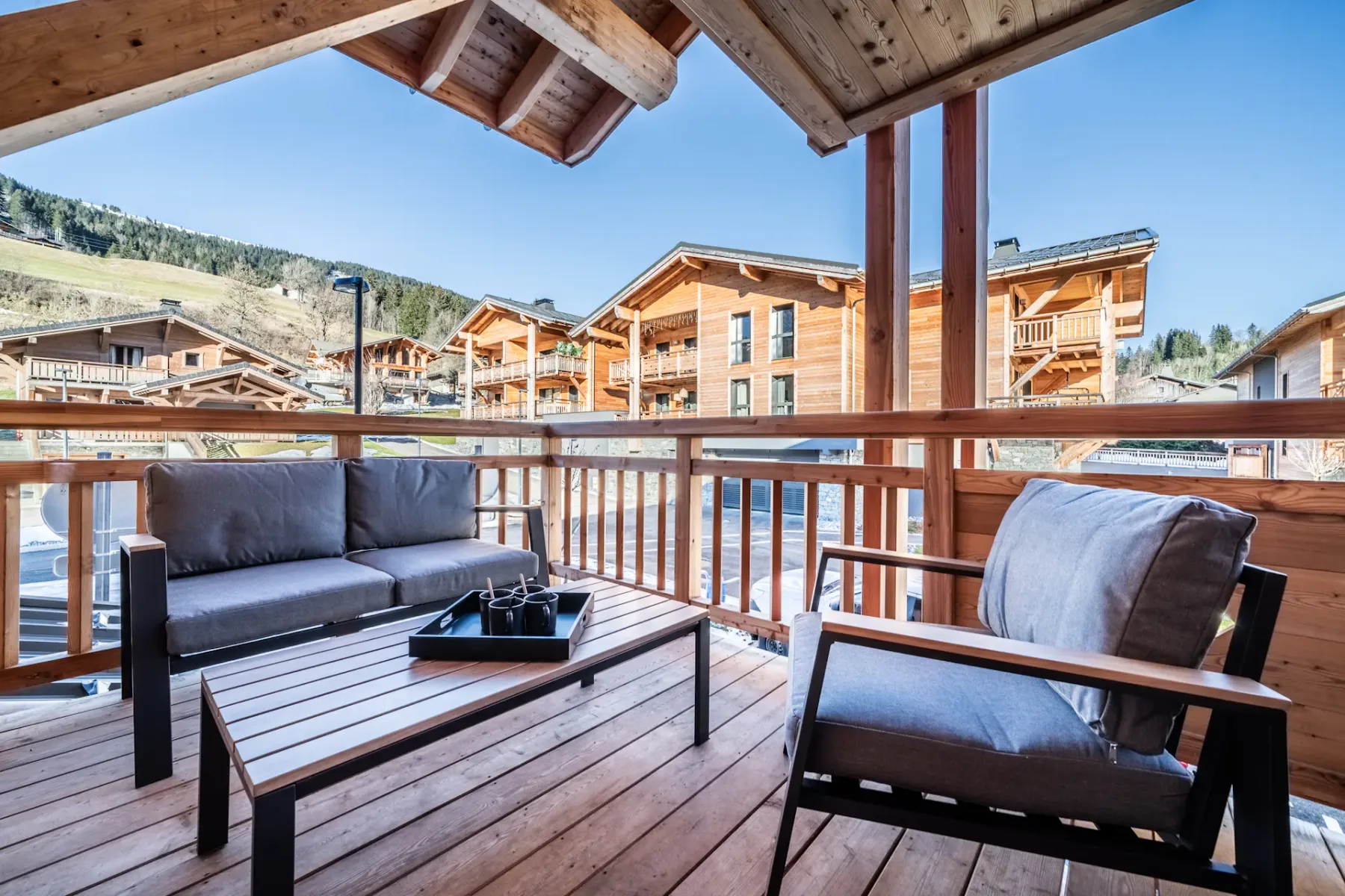 A covered wooden terrace with cushioned seating and views of nearby buildings.