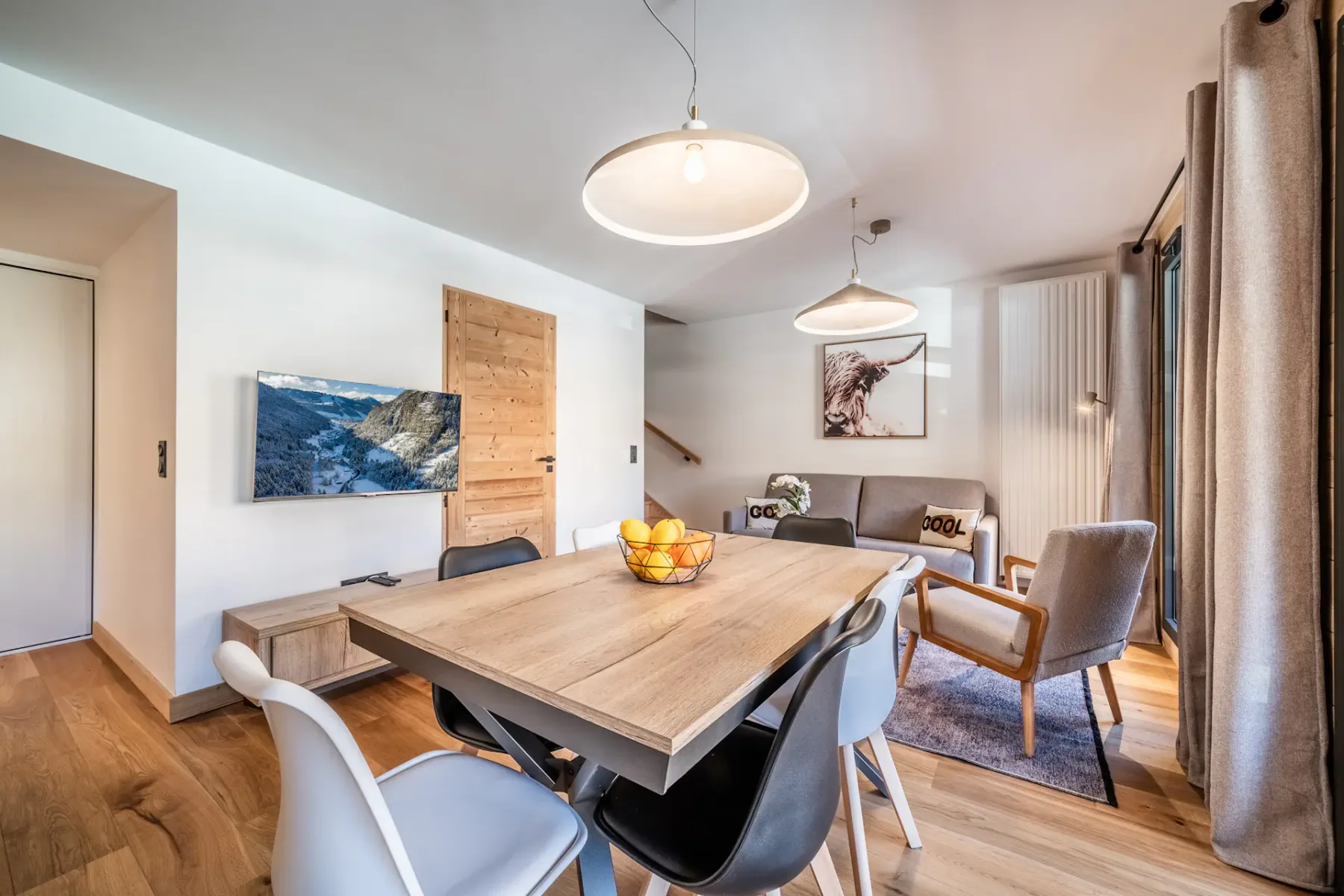 A dining area with a wooden table, chairs, and a wall-mounted television.