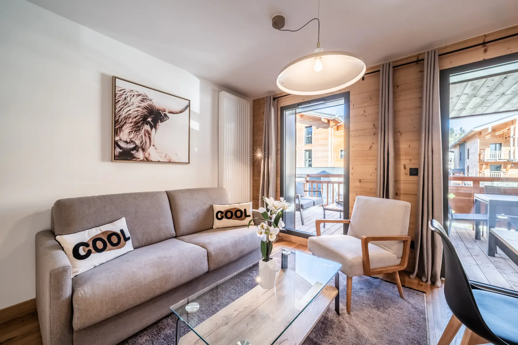 A living room with a sofa, a glass coffee table, and large windows.