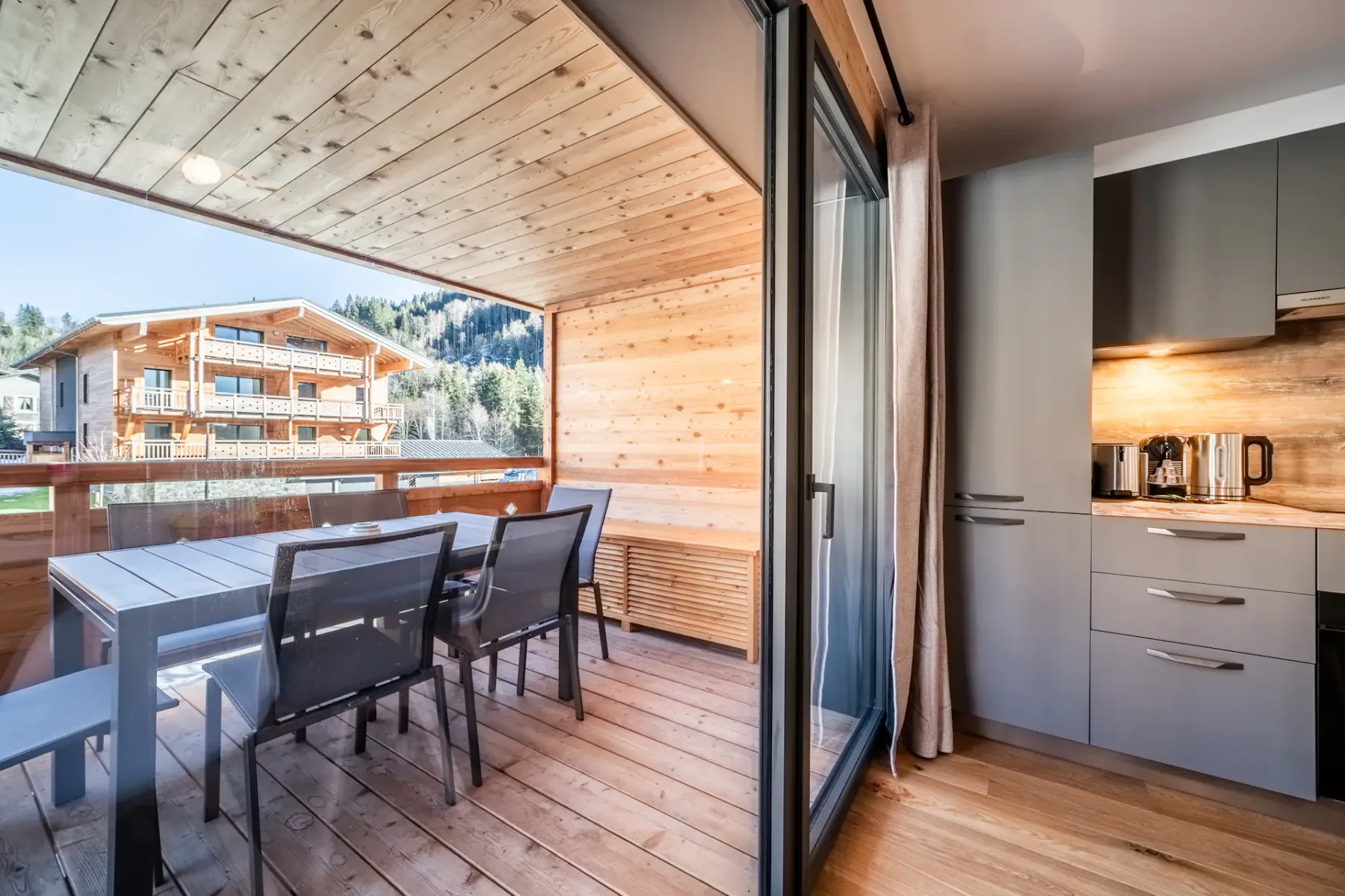 A balcony dining area with a table and chairs beside a compact kitchen.