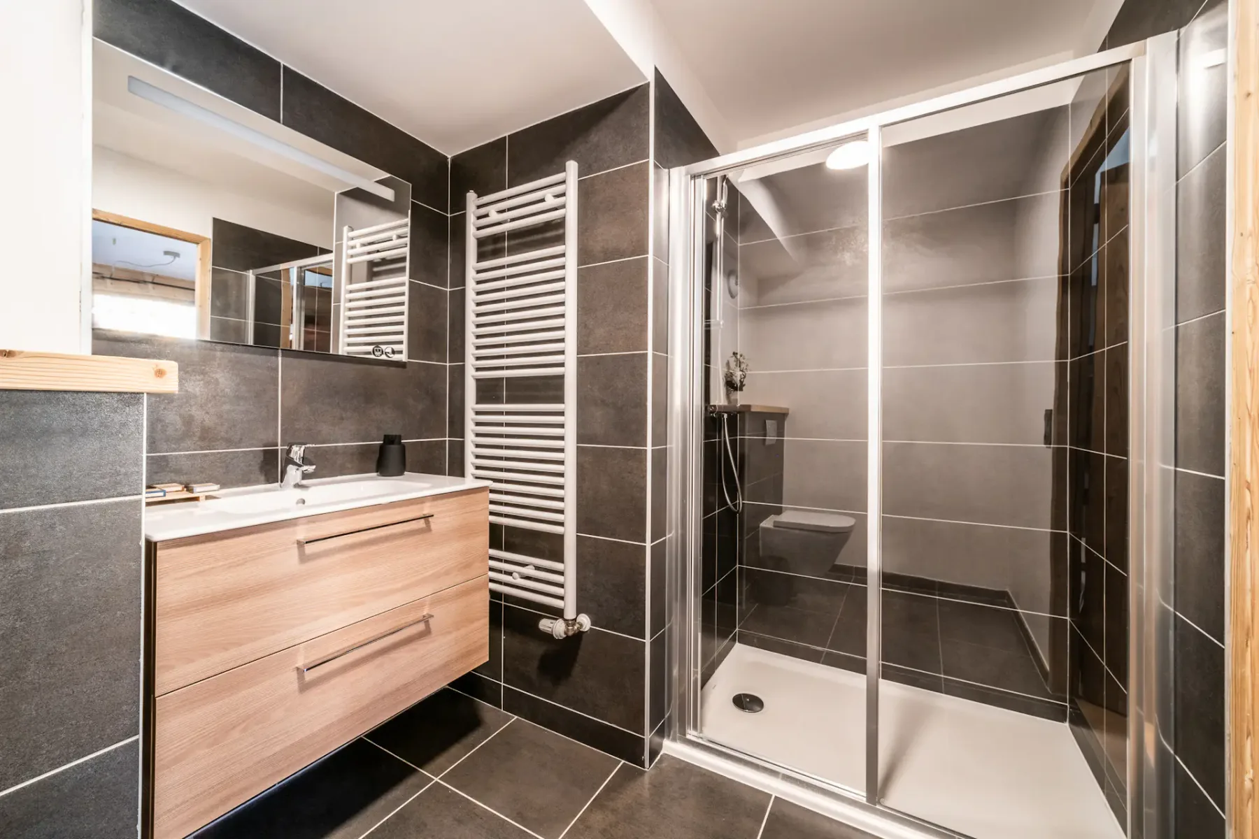 A bathroom with a wood-toned vanity, wall mirror, and glass shower.