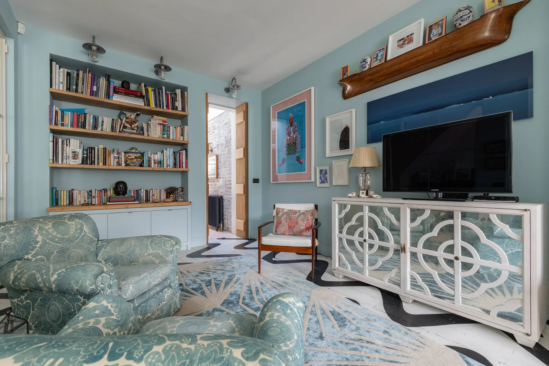 Una sala de estar con asientos estampados, estanterías y un televisor sobre un mueble.