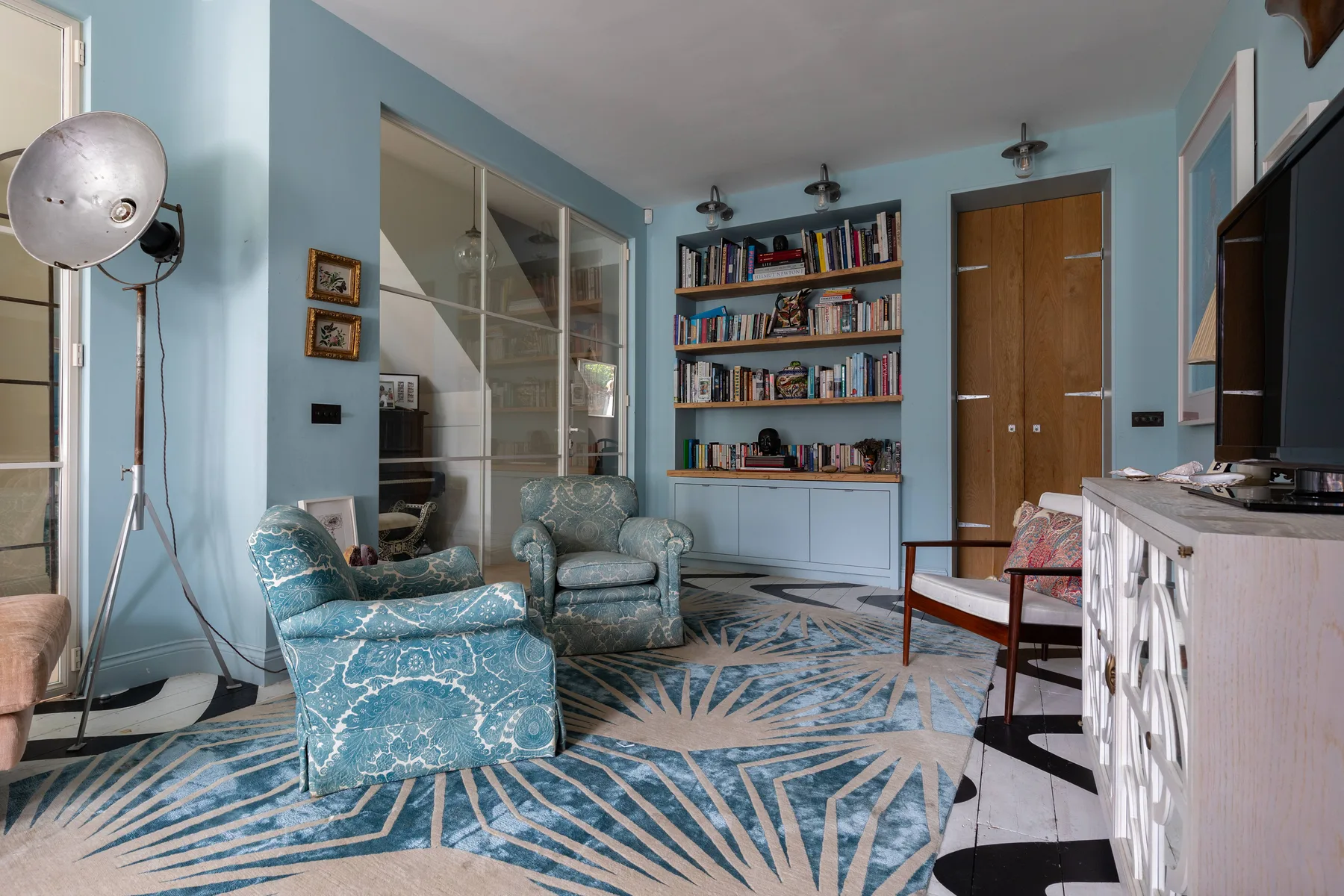Una sala azul con asientos estampados y una pared de estanterías.