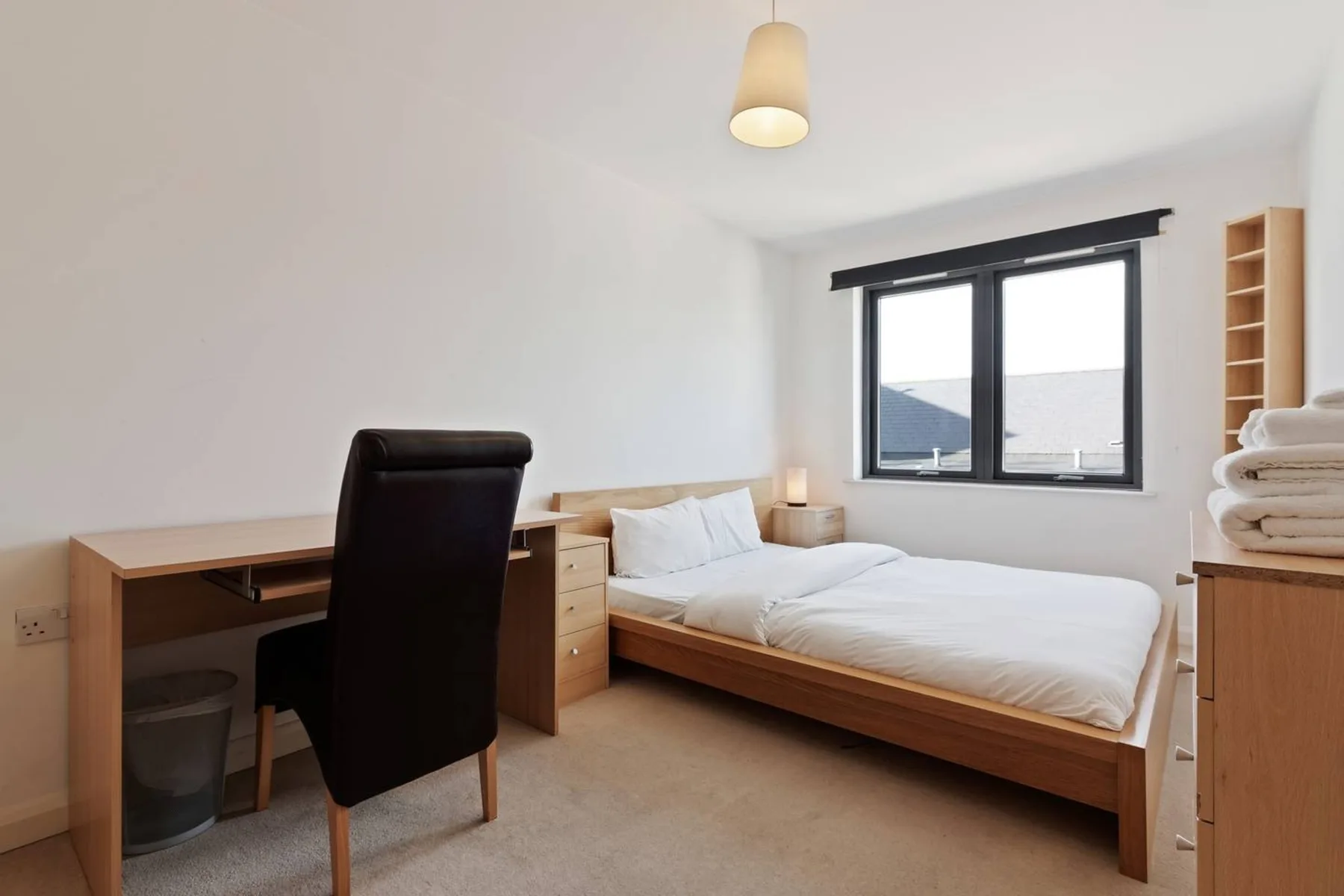 Un dormitorio luminoso con cama, escritorio y ventana.