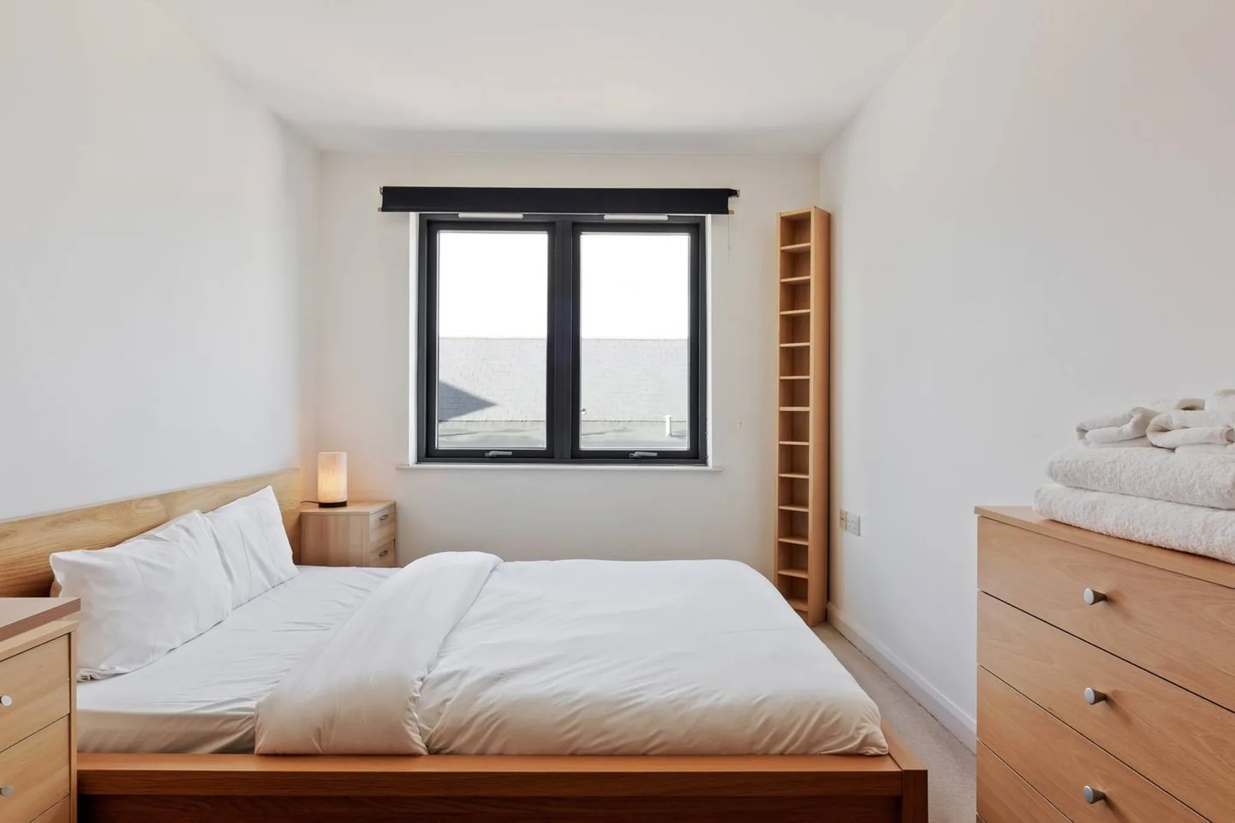 A bright bedroom with a bed, a window, and wooden furnishings.