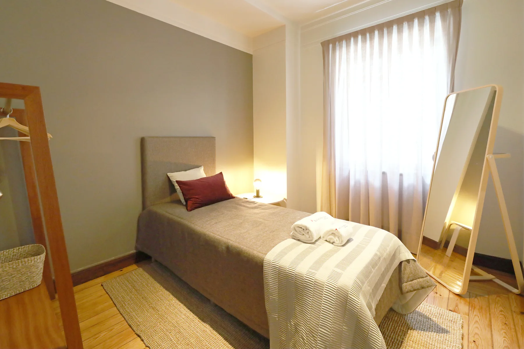 A bedroom with a single bed, bedside lamp, and full-length mirror.