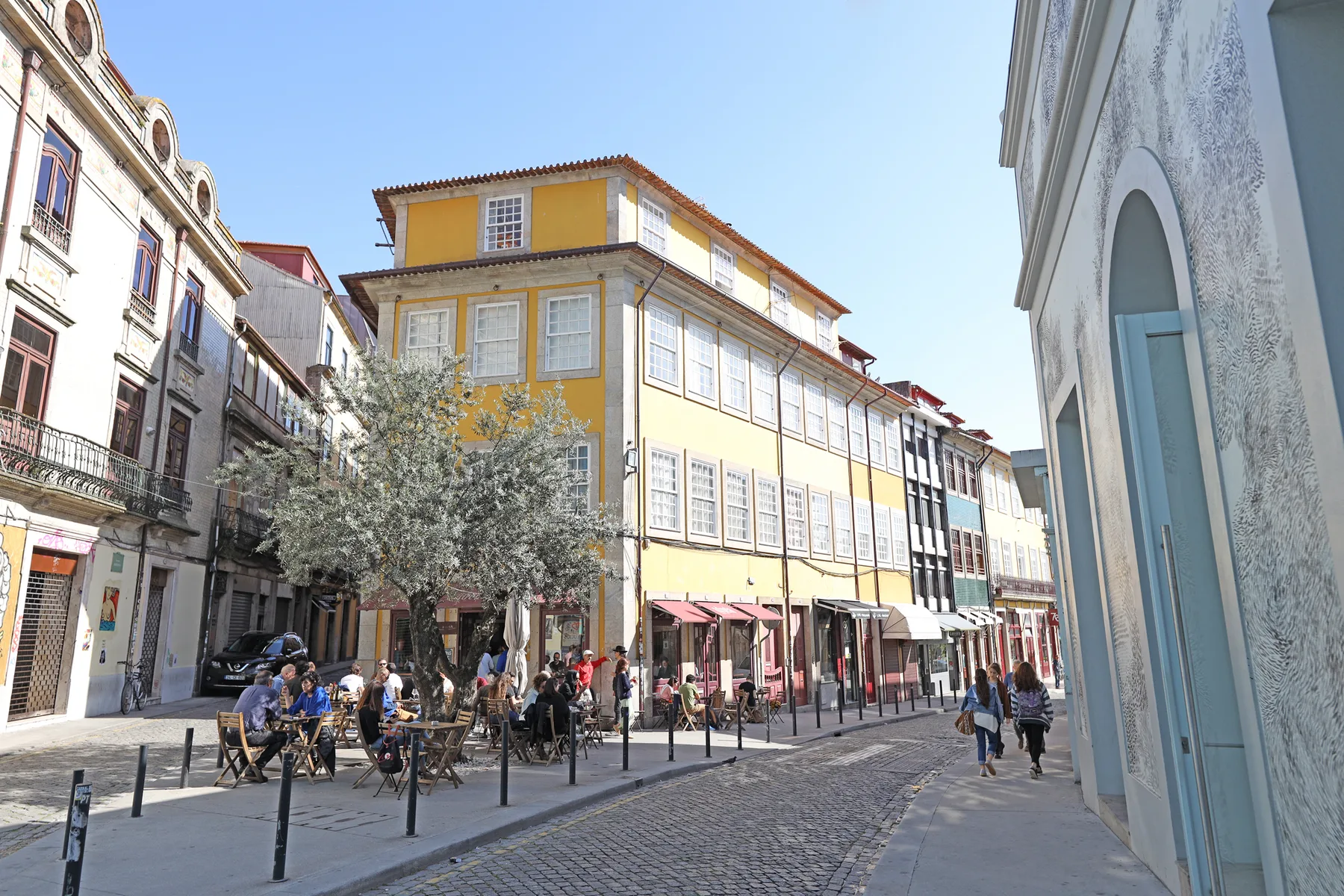 Una calle adoquinada bordeada de edificios coloridos y mesas de café al aire libre.