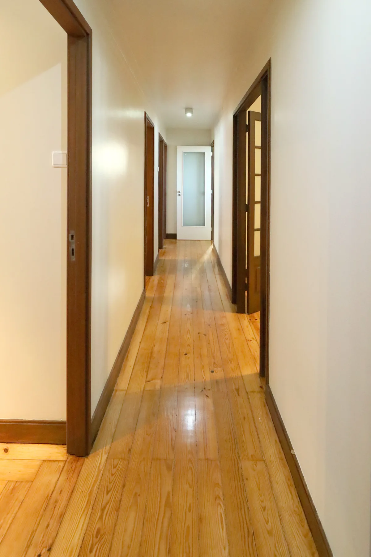 Un pasillo con suelo de madera y varias puertas.
