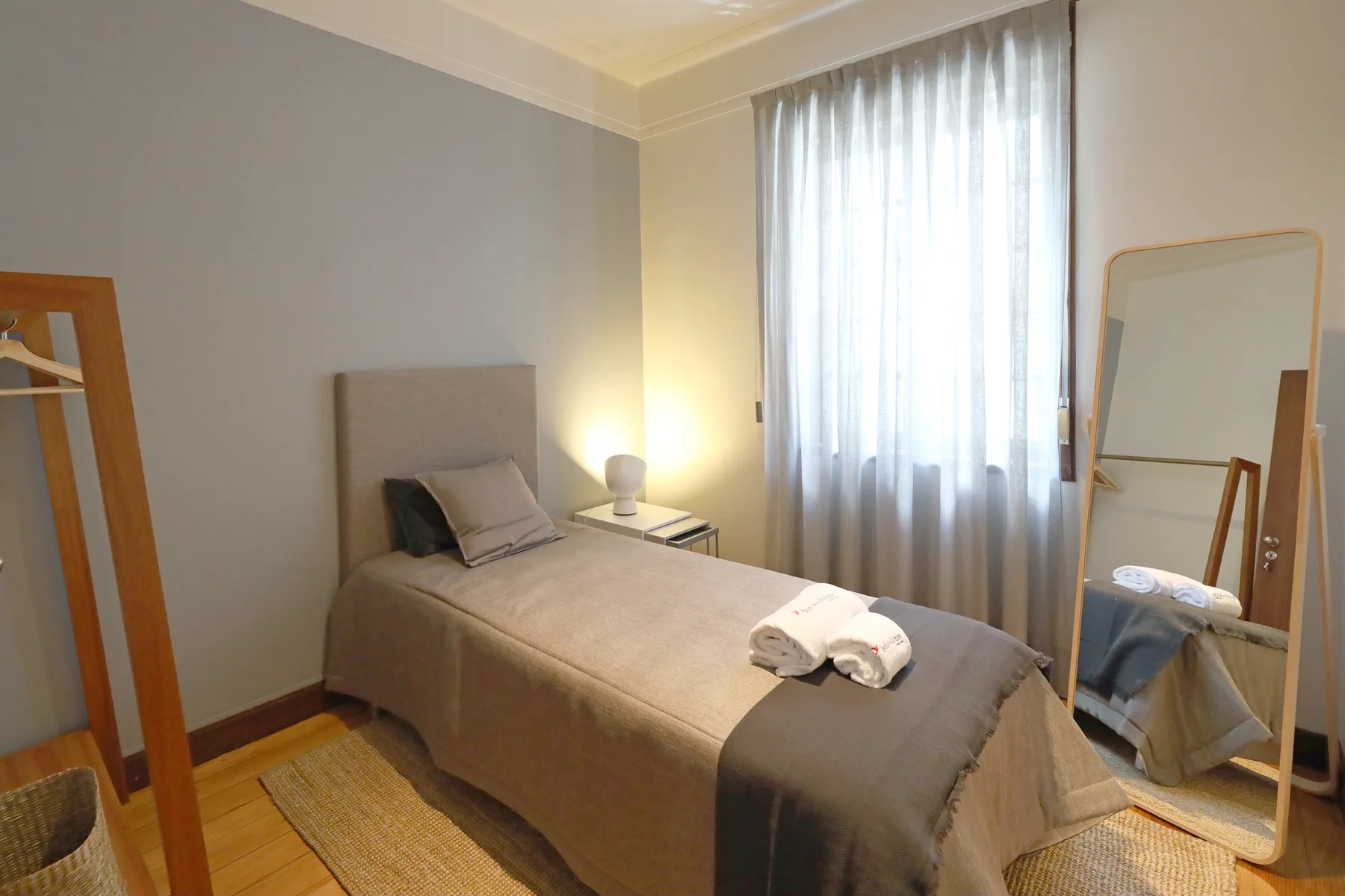 A bedroom with a neatly made bed beside a tall curtained window.