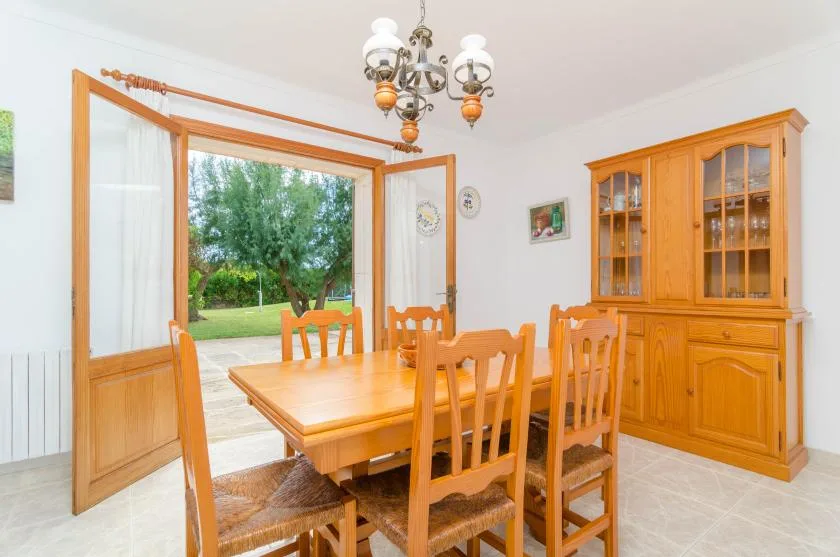 Una mesa de comedor de madera y sillas están junto a puertas abiertas con vistas al jardín.