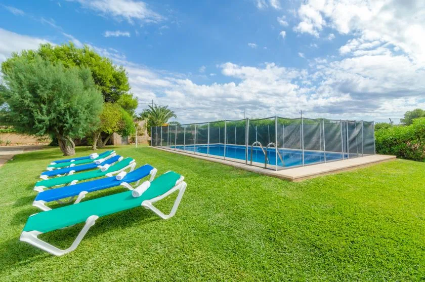 Una piscina al aire libre está junto a un césped con tumbonas en fila.