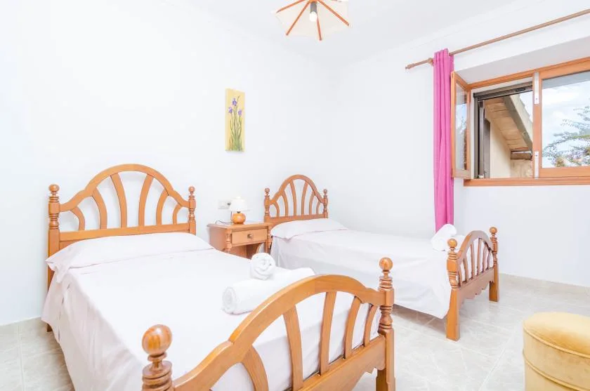 Un dormitorio luminoso con dos camas de madera y una ventana con cortinas rosas.
