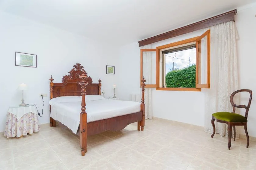 Un dormitorio con una cama de madera y una ventana abierta con vistas a la vegetación.
