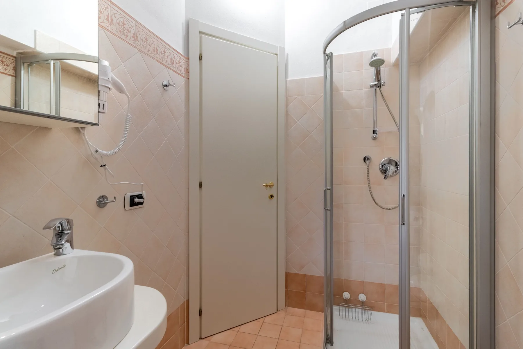 Un baño alicatado con lavabo, espejo y ducha de vidrio.