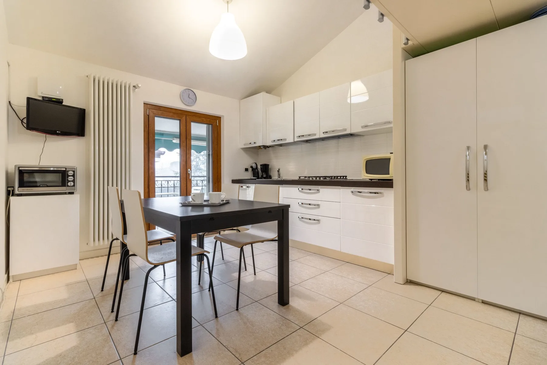 Una cocina con zona de comedor, armarios blancos y una mesa.
