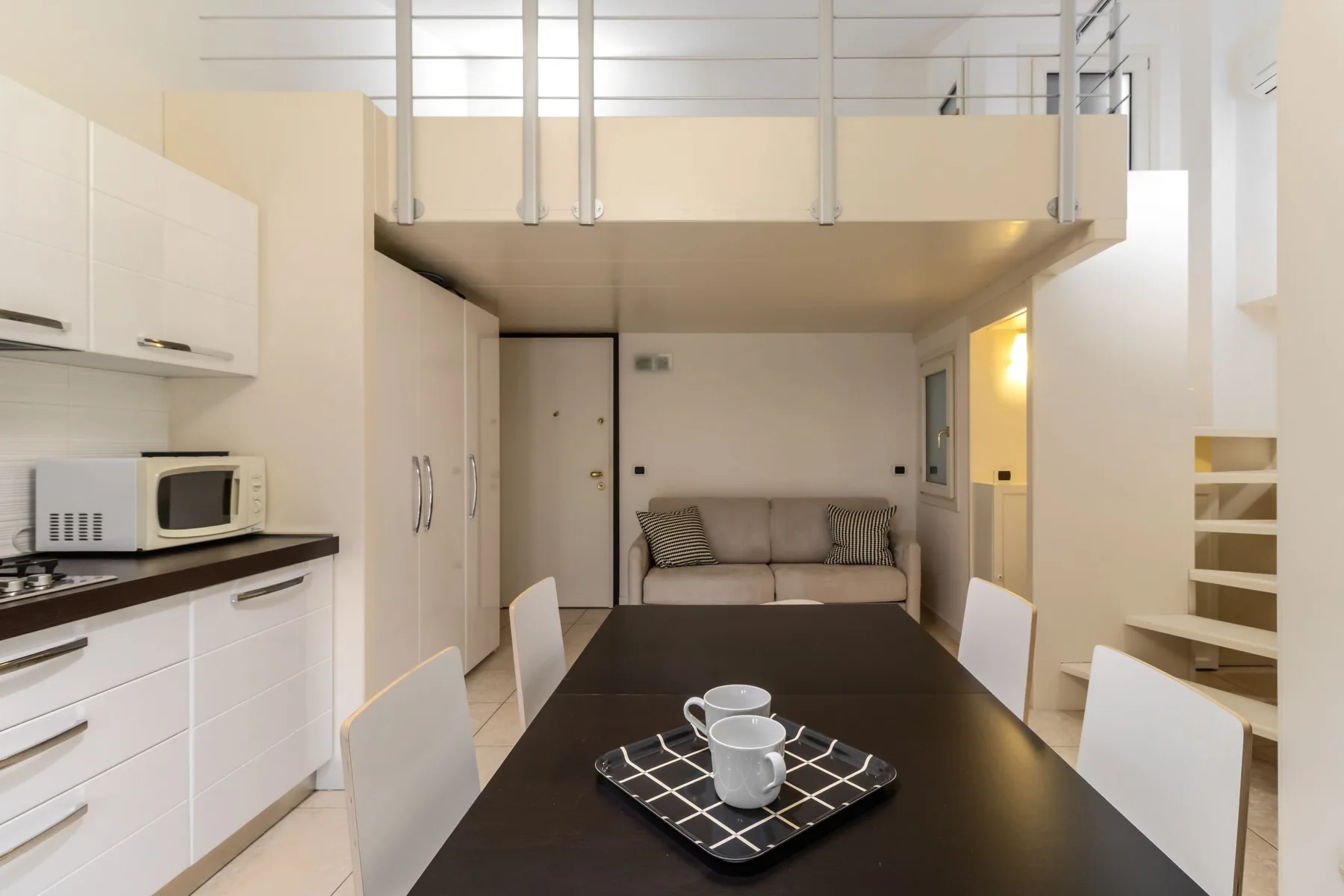 Una luminosa sala-comedor diáfana con una mesa y asientos bajo un altillo.