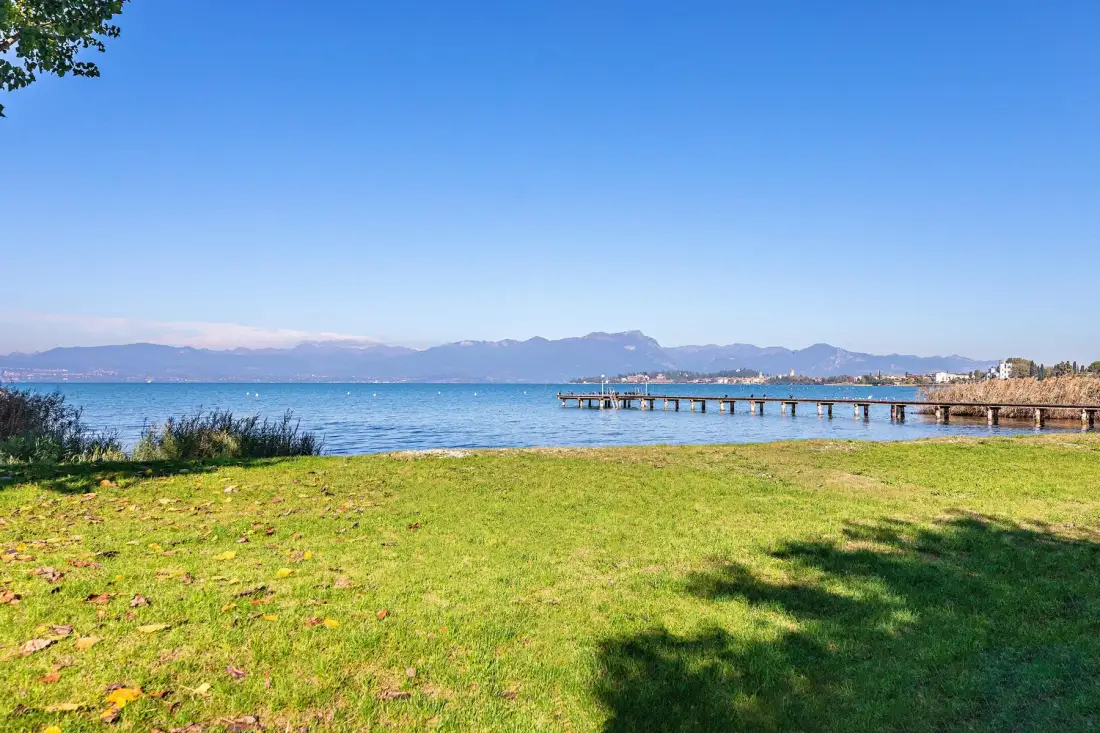 Un césped junto al agua mira hacia aguas azules, con un muelle que se extiende por la orilla.