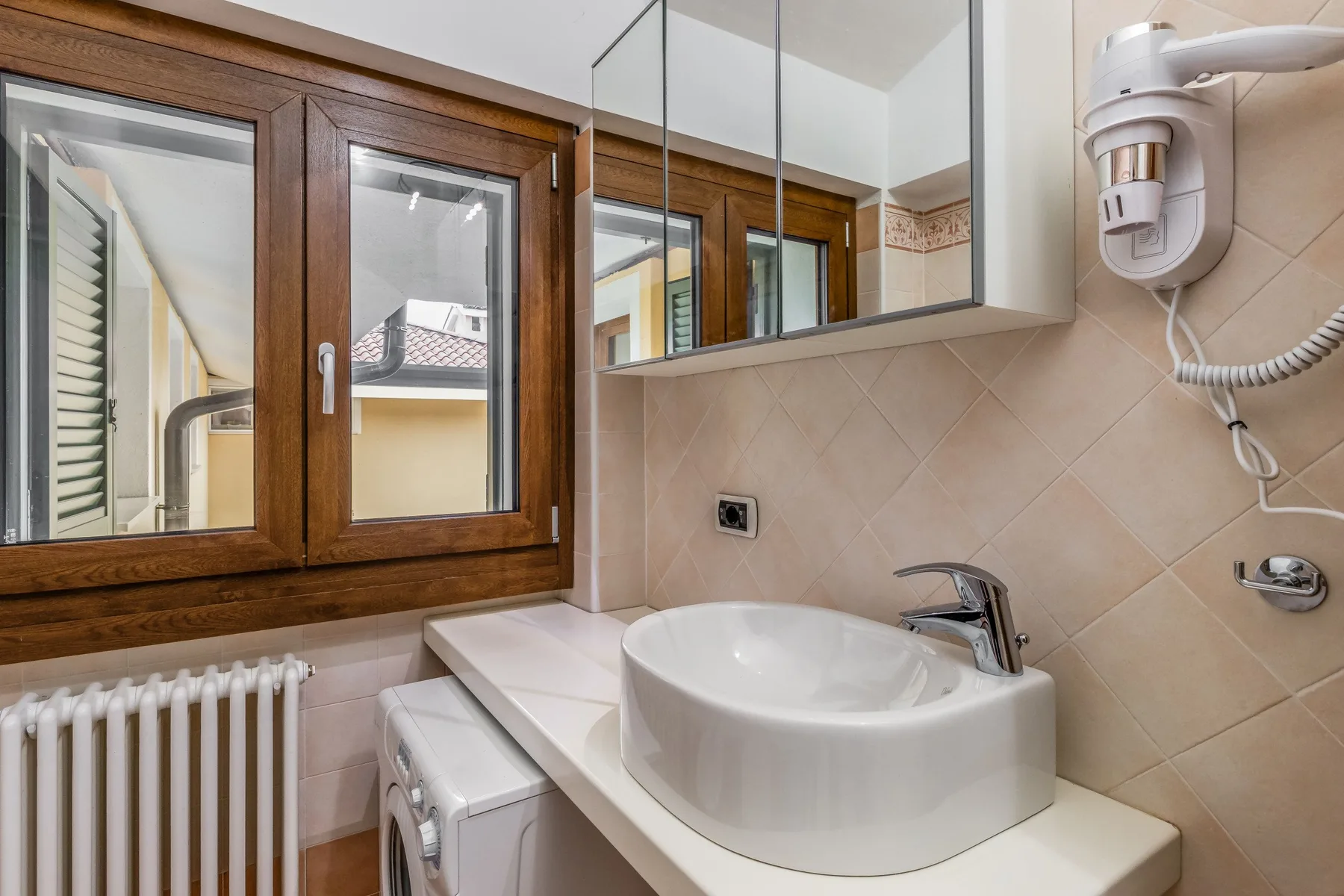 Un baño con lavabo, espejo de pared y ventana con marco de madera.
