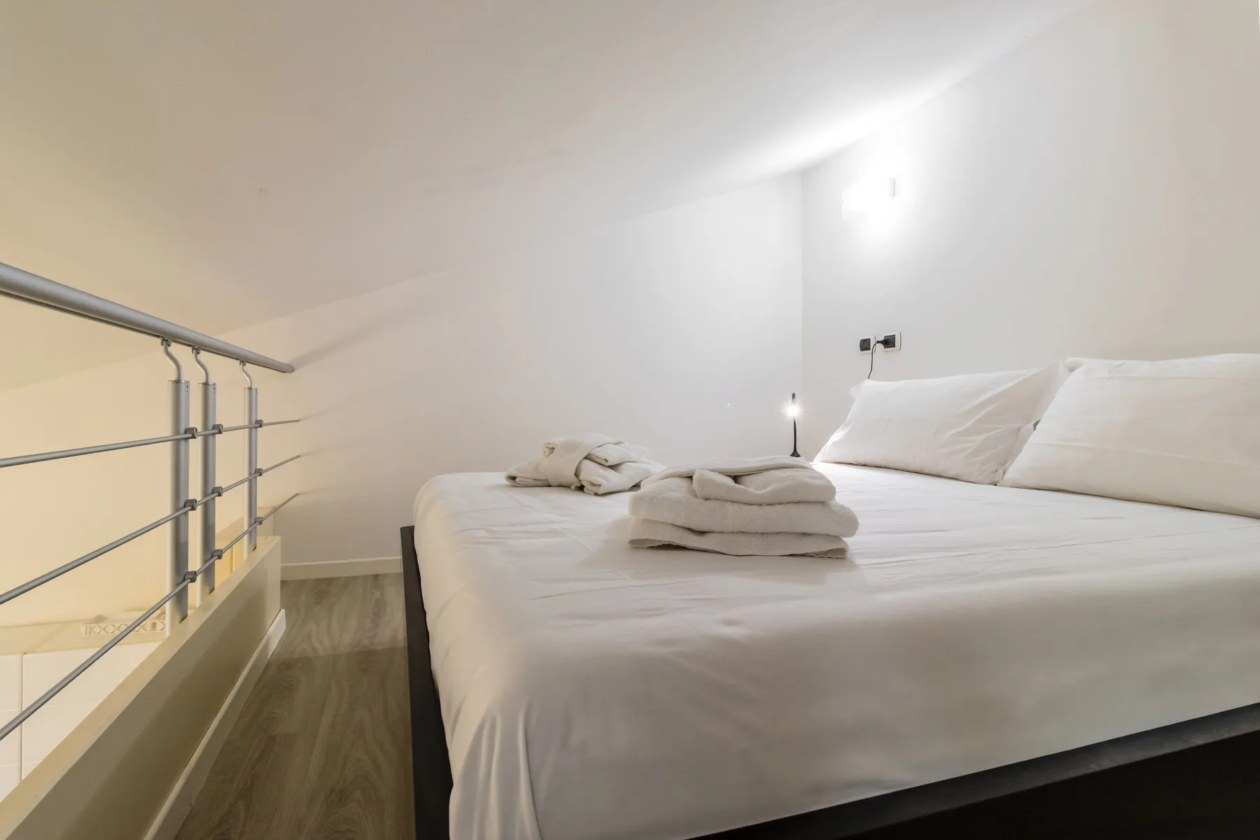 Un dormitorio con una cama y toallas dobladas junto a una barandilla metálica.