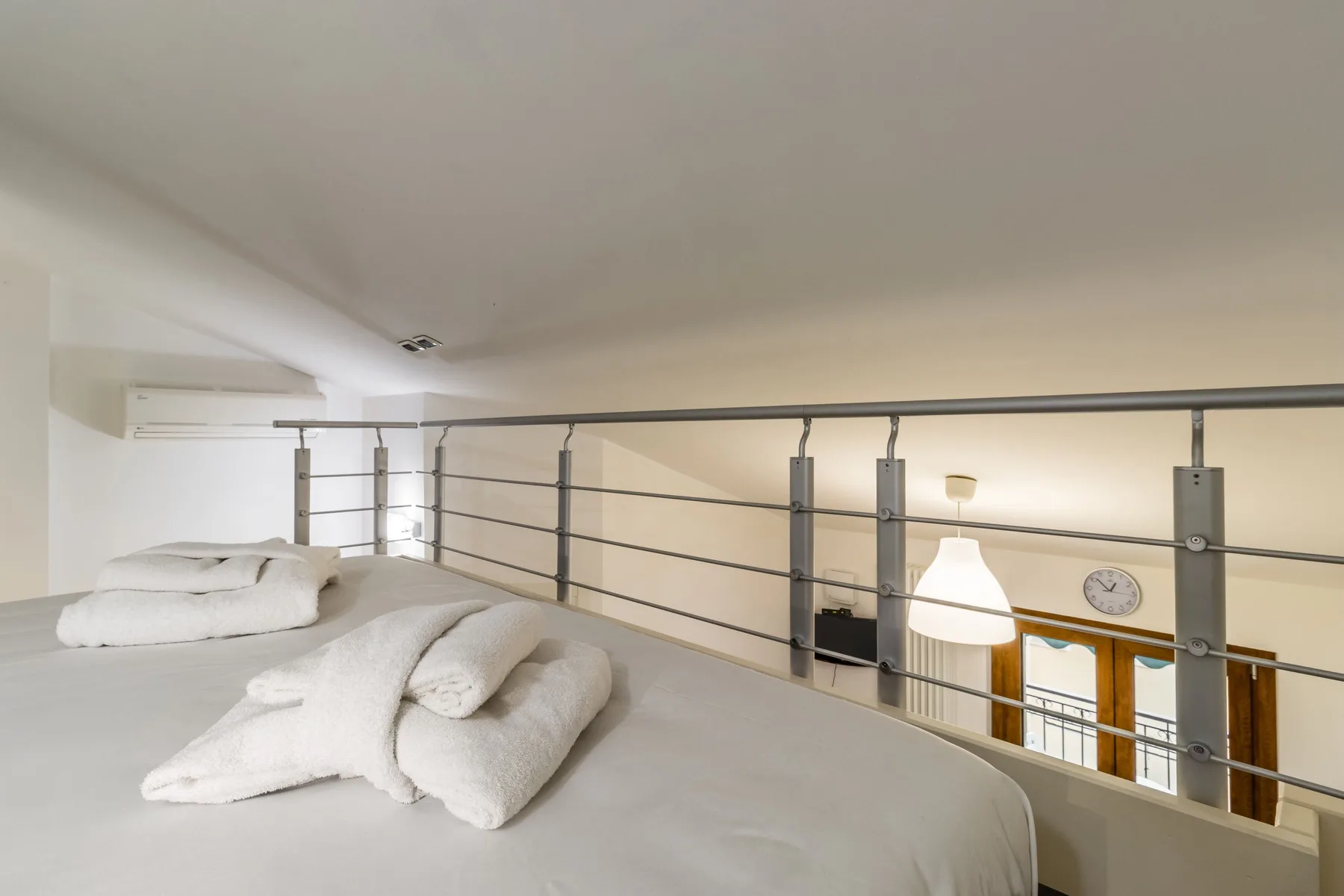 Una zona de descanso tipo loft da a una sala a través de una barandilla metálica.
