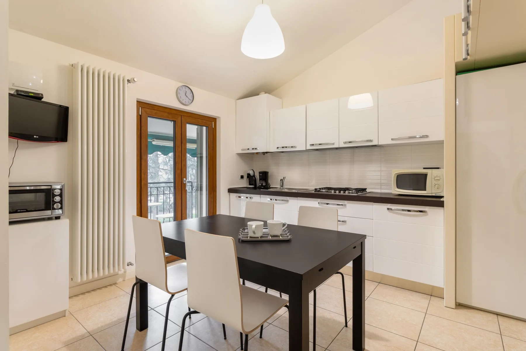 Una cocina luminosa con comedor, una mesa oscura y muebles blancos.