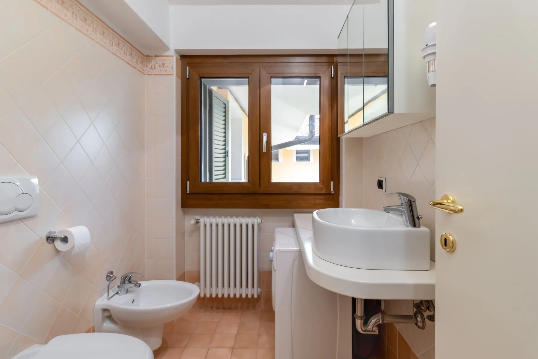 Un baño alicatado con lavabo, bidé, inodoro y ventana.