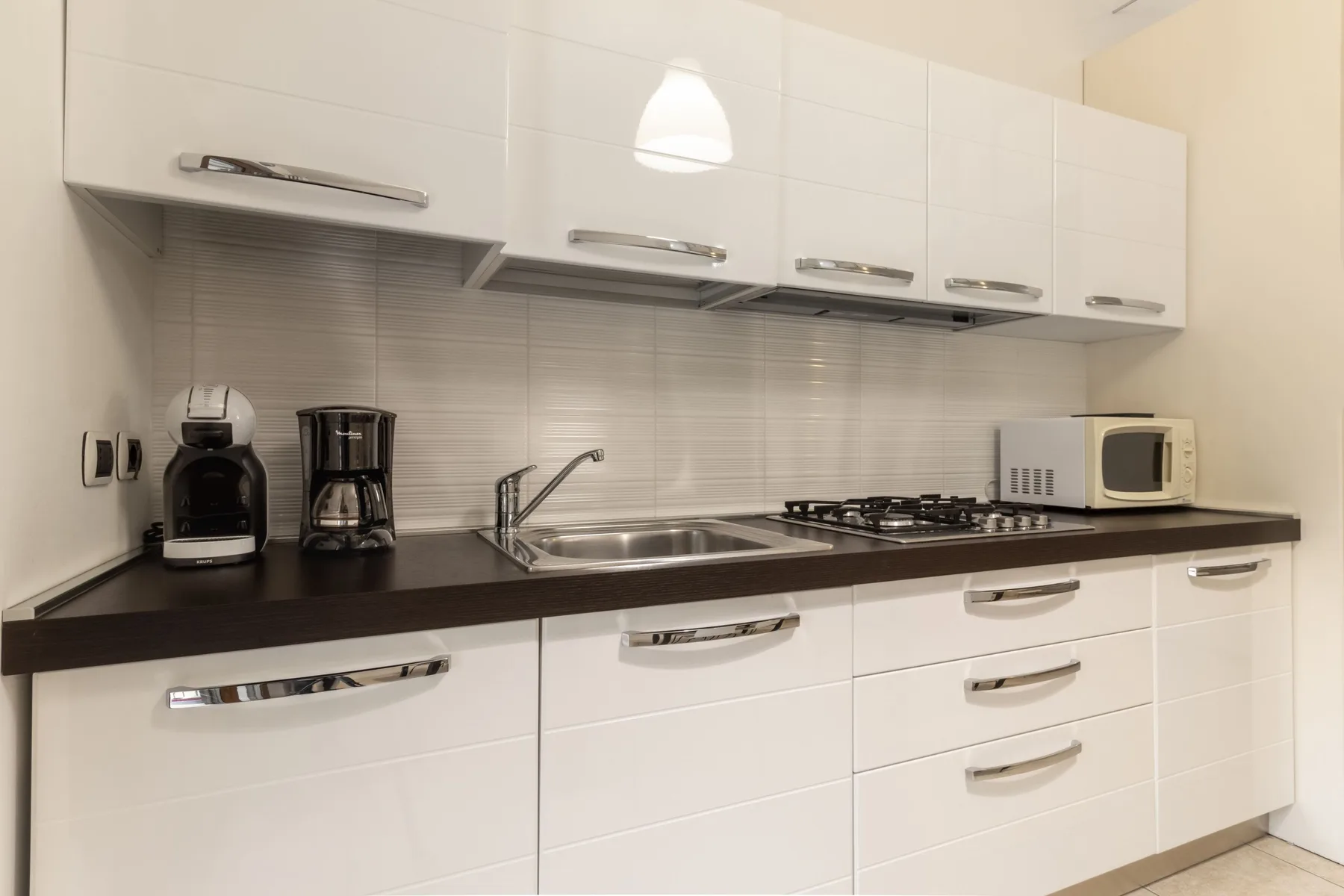 Una cocina luminosa con gabinetes blancos, una encimera oscura y electrodomésticos.