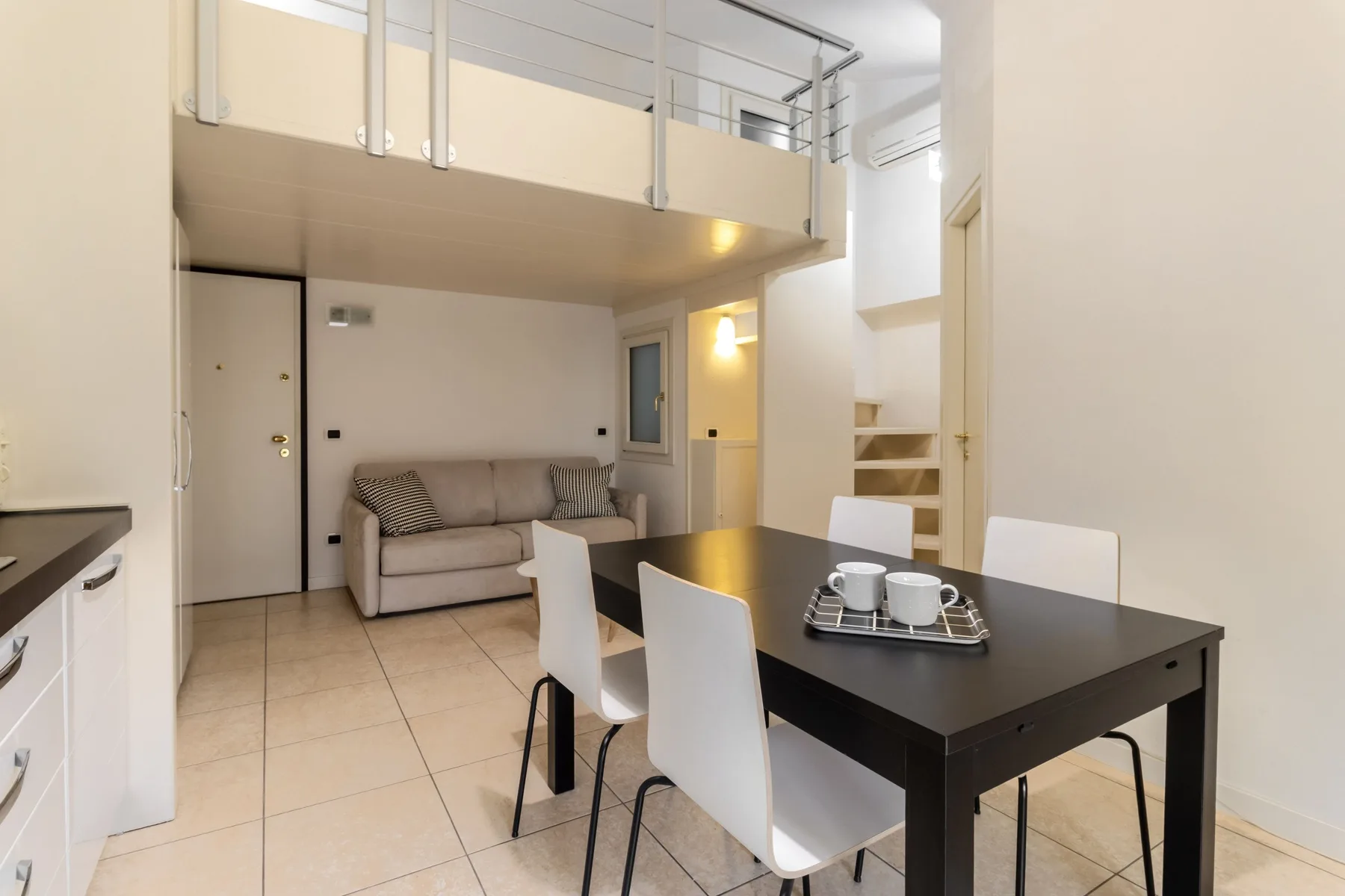 Una luminosa zona abierta de comedor y sala de estar, con mesa y asientos bajo un altillo.