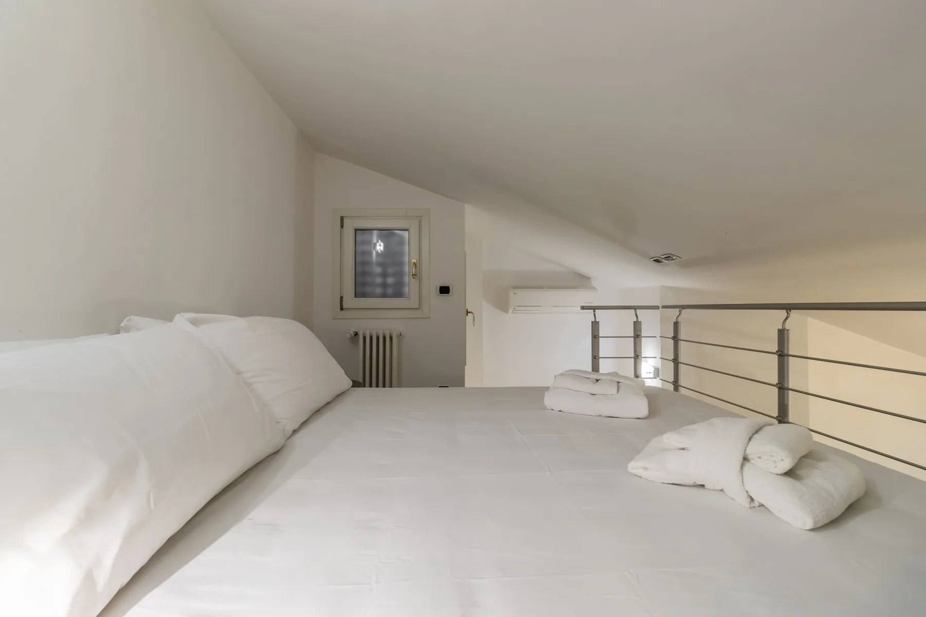 Un dormitorio con una cama blanca bajo un techo inclinado.