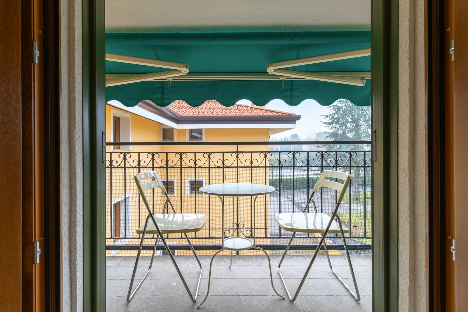Una pequeña zona de estar en un balcón bajo un toldo verde da a un edificio cercano.
