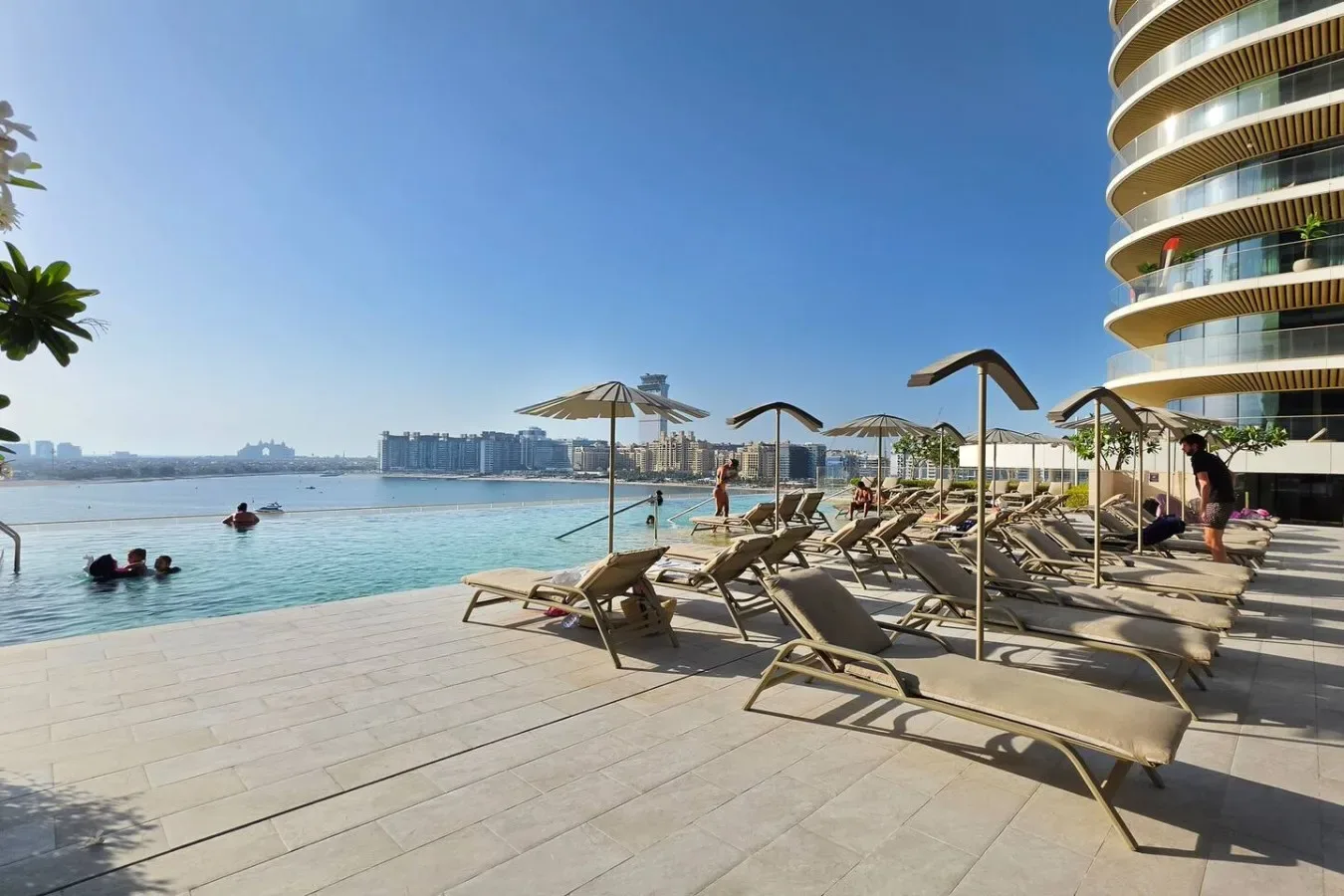 Una terraza junto a la piscina con asientos mira al agua y a edificios lejanos.