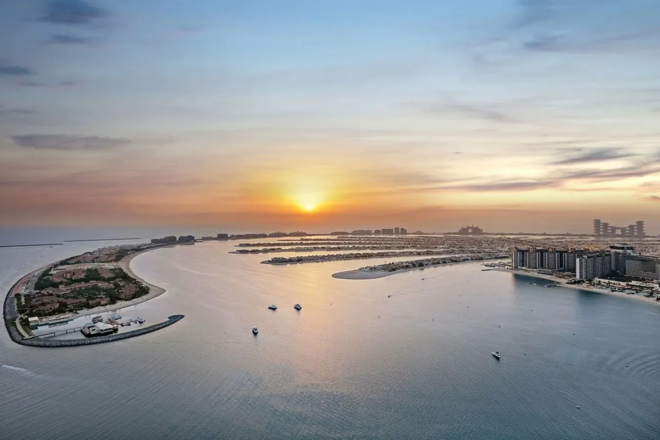 Vista aérea de un desarrollo frente al agua al atardecer, con formas curvas que se extienden sobre el agua.