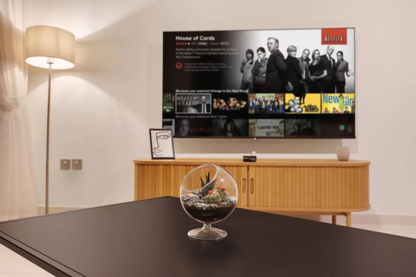 Una sala de estar con un televisor sobre un mueble de madera y un centro de mesa de vidrio.