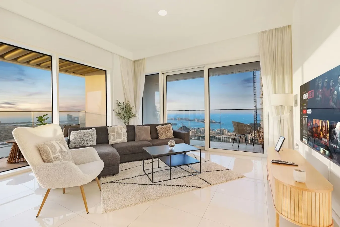 Una sala de estar luminosa con asientos, una mesa de centro y grandes ventanas con vistas al mar.