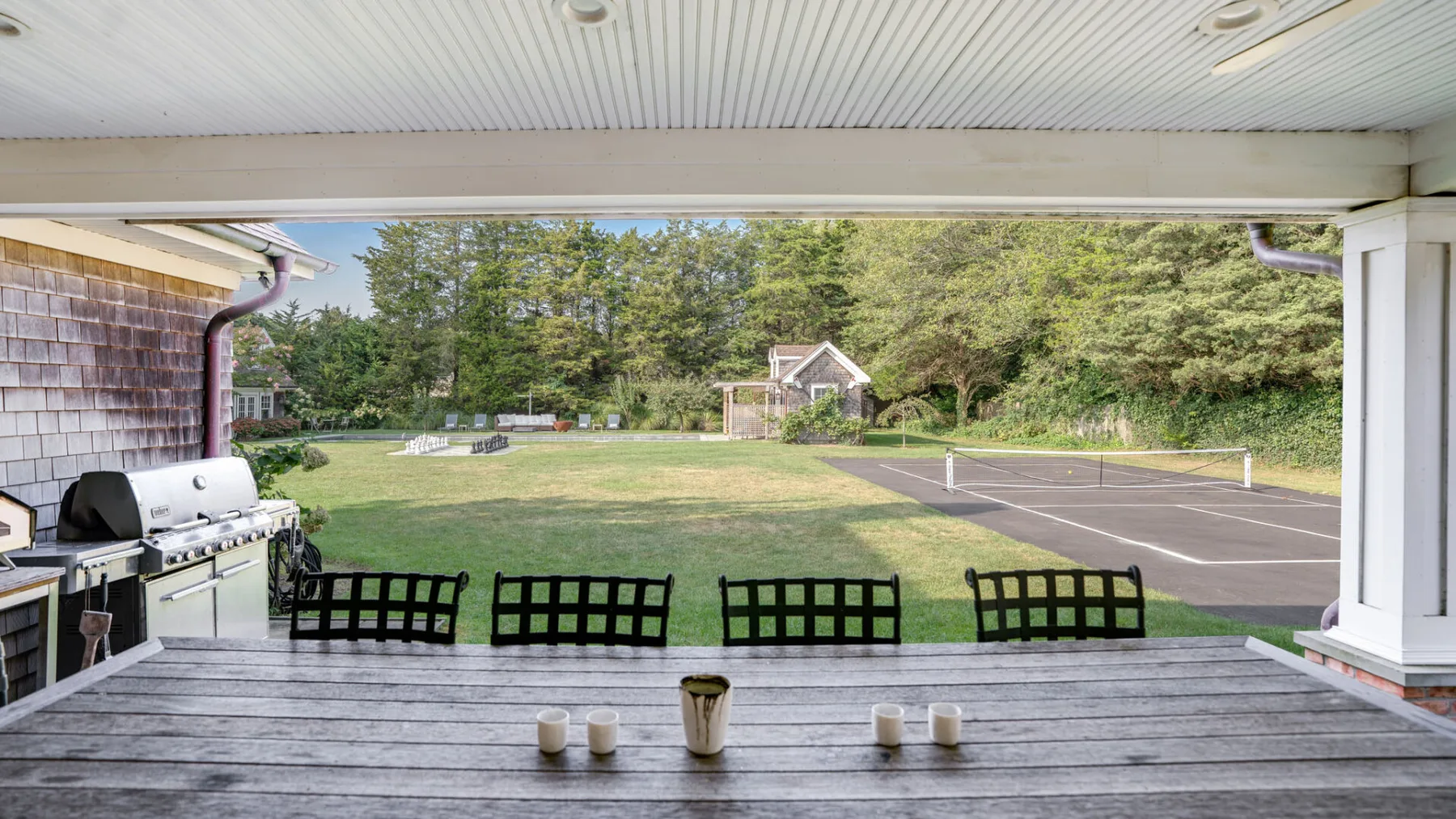 A covered outdoor patio overlooks a lawn and tennis court.