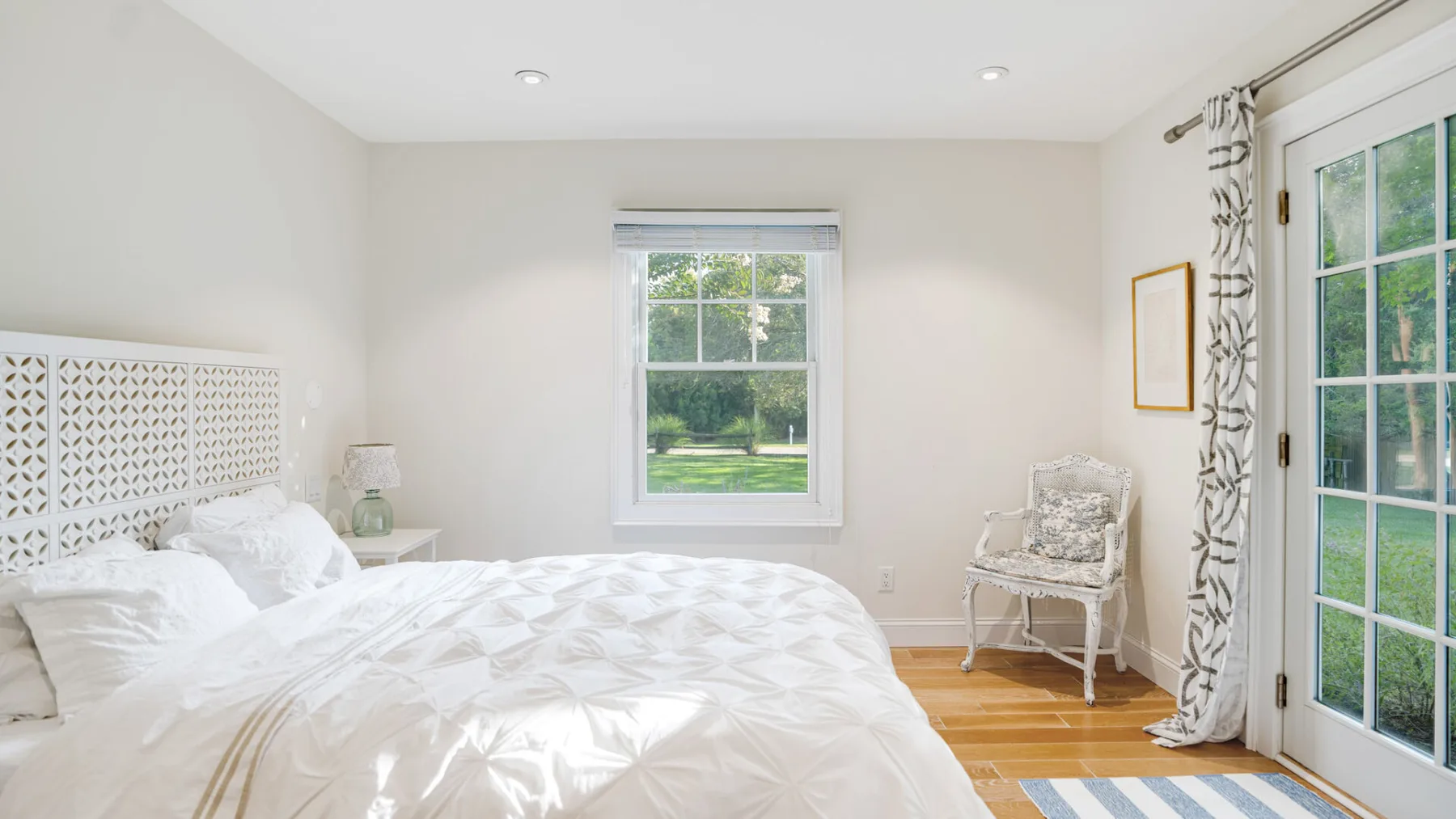 A bright bedroom with a bed beside a window and glass doors.