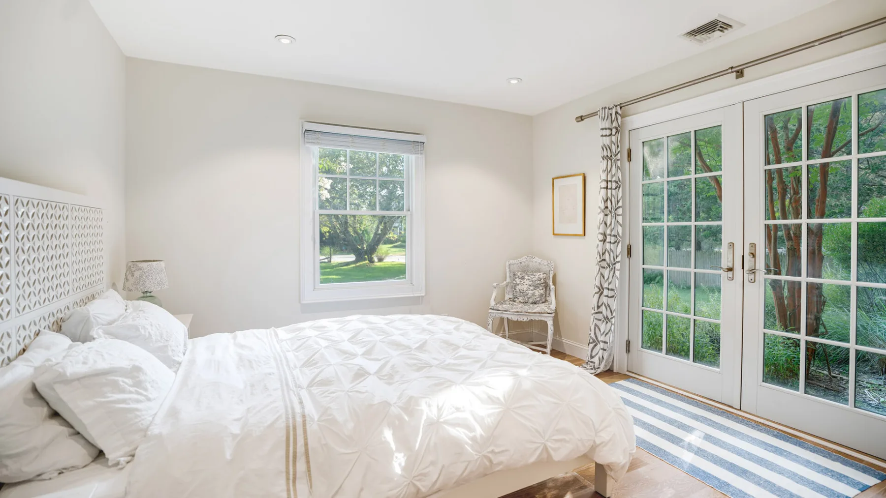 A bright bedroom with a neatly made bed and glass doors opening onto greenery.