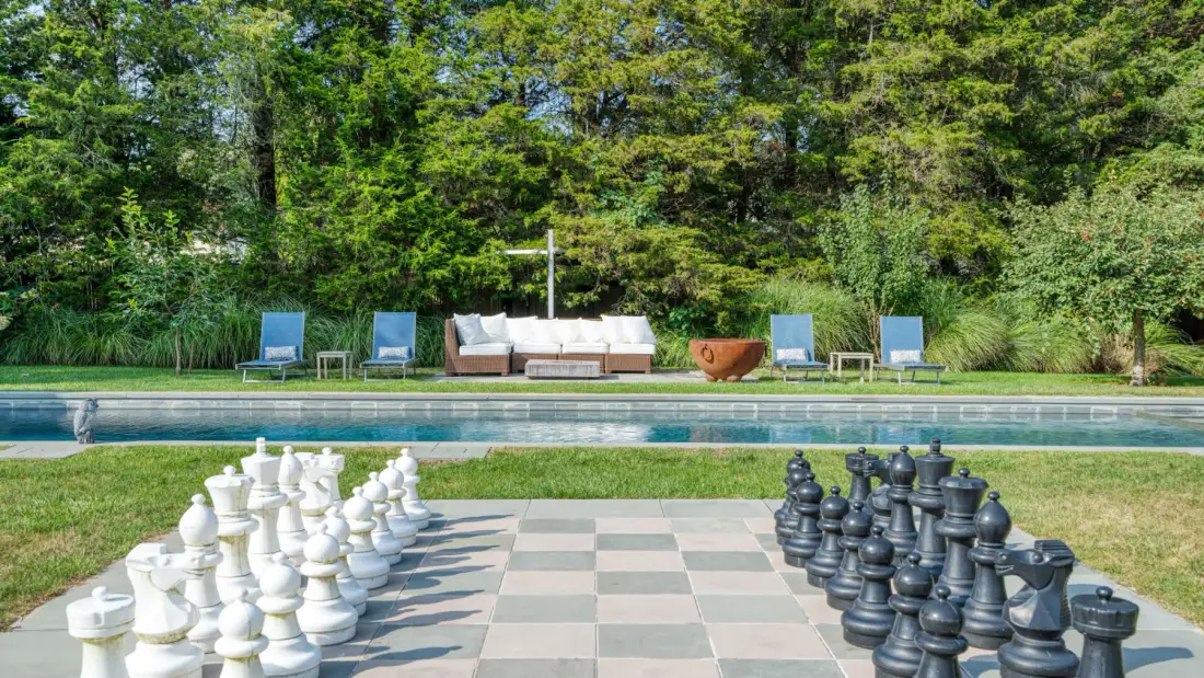 An outdoor chess area with oversized pieces beside a swimming pool.