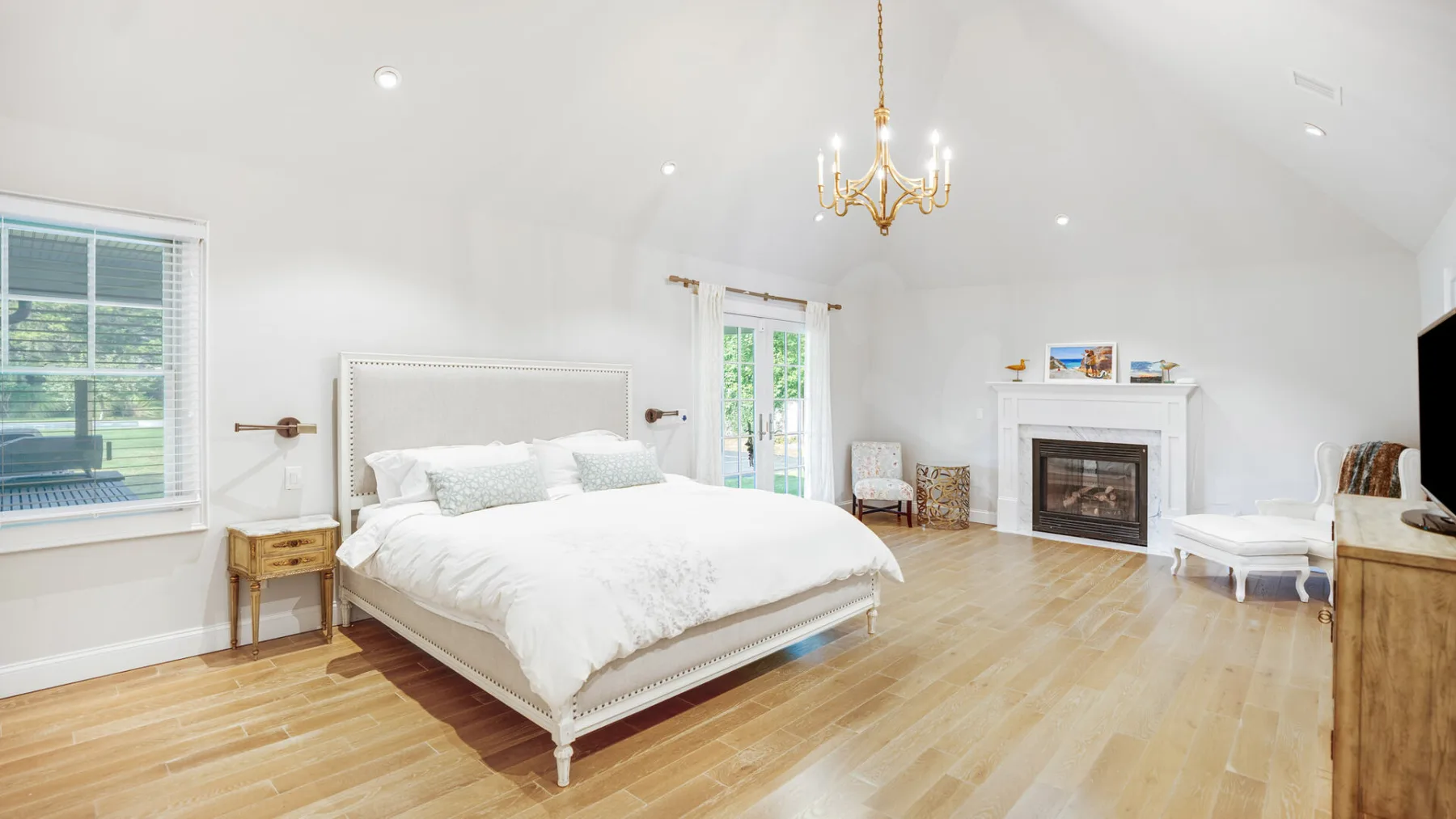 A bright bedroom with a large bed and a fireplace.