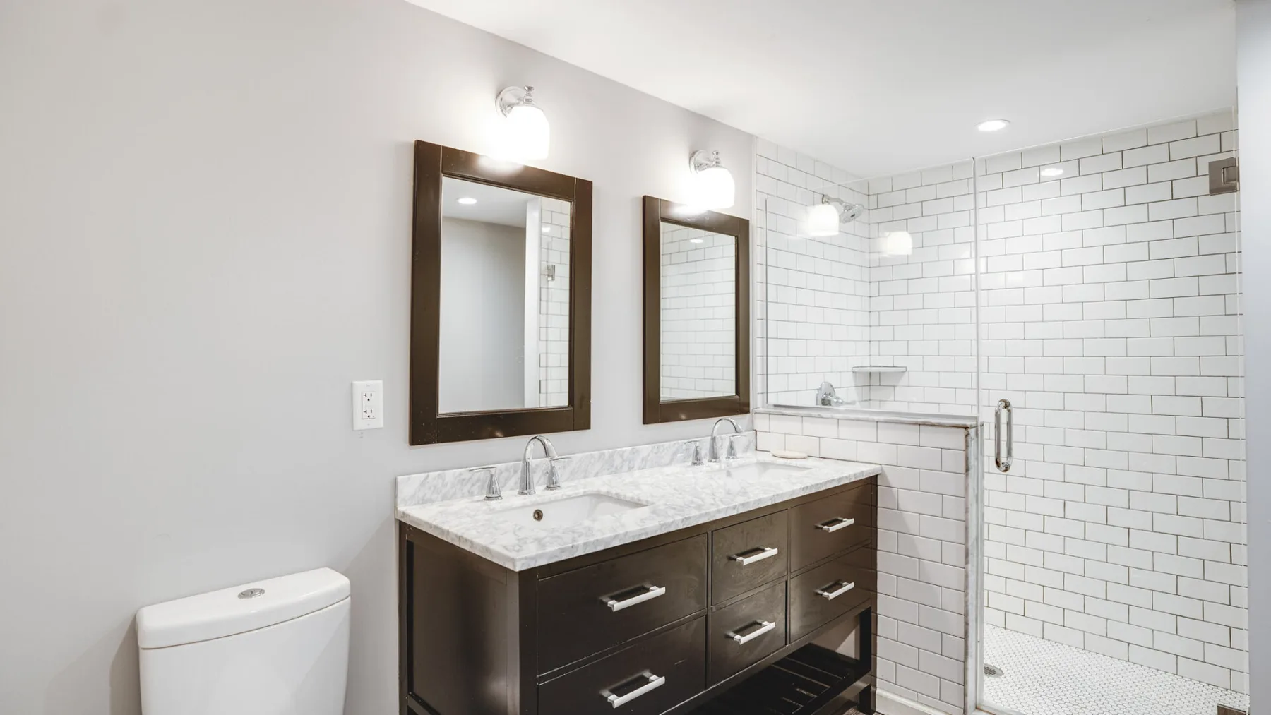 A bathroom with a dark vanity, two mirrors, and a tiled shower.