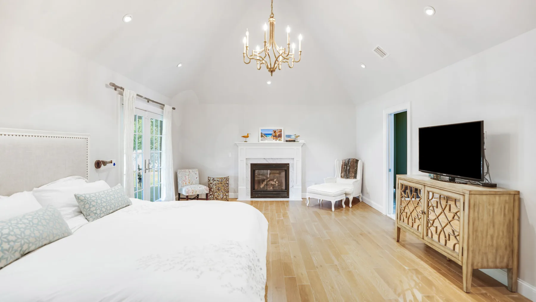 A bright bedroom with a bed, fireplace, and television.