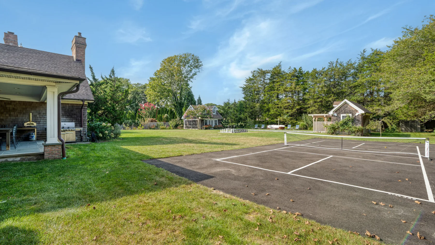 Una cancha de tenis está junto a un césped ajardinado y árboles.