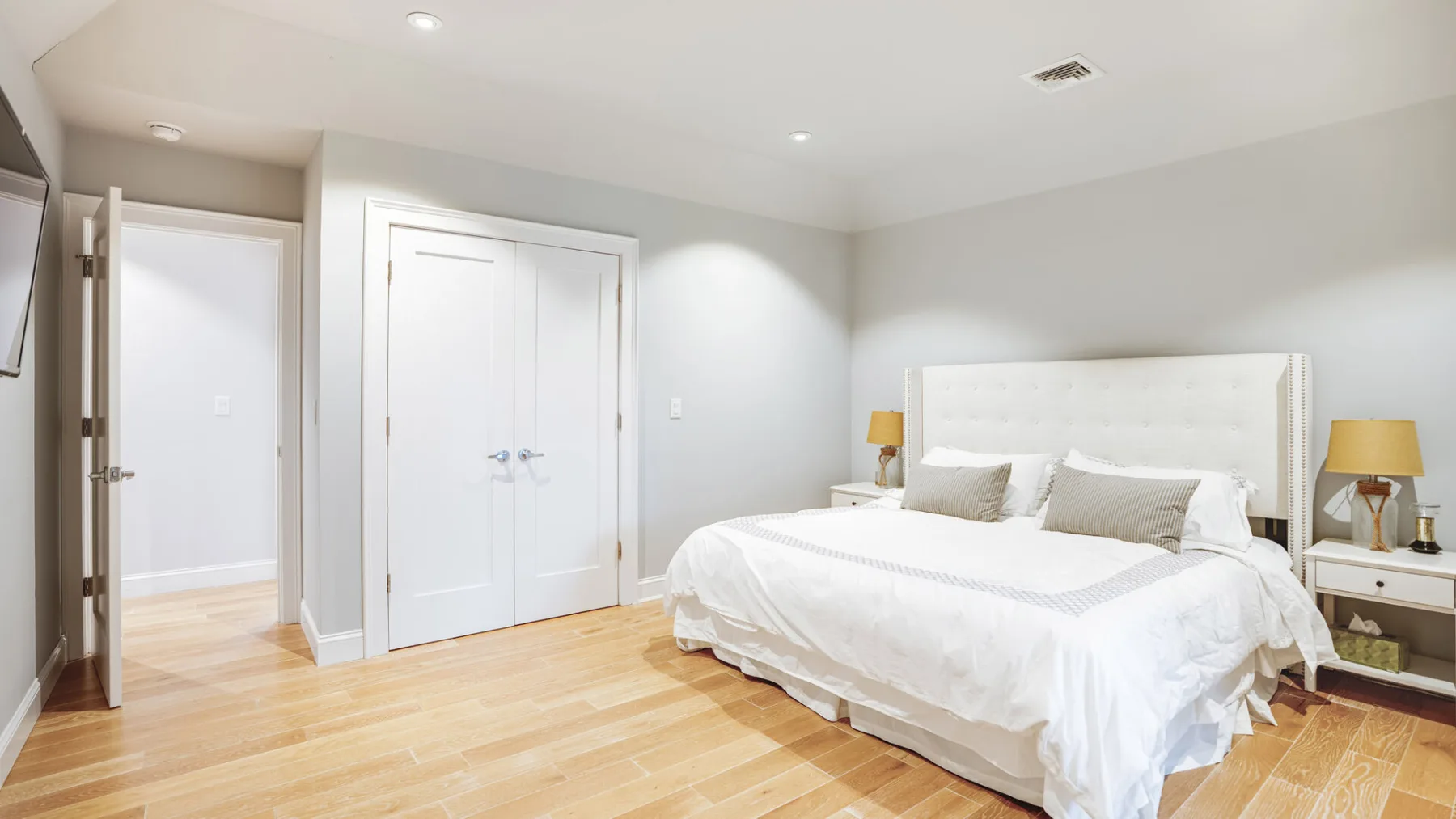 A bright bedroom with a bed, white bedding, and light wood flooring.