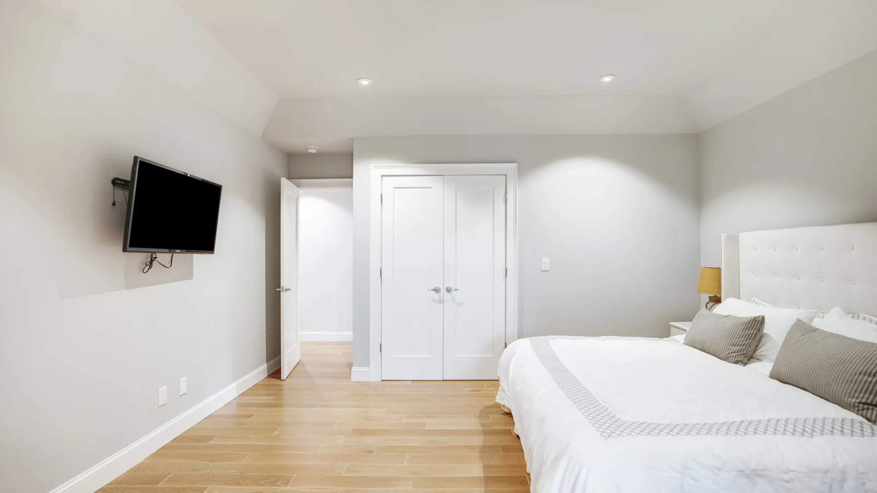 A bright bedroom with a bed, wall-mounted television, and white double doors.