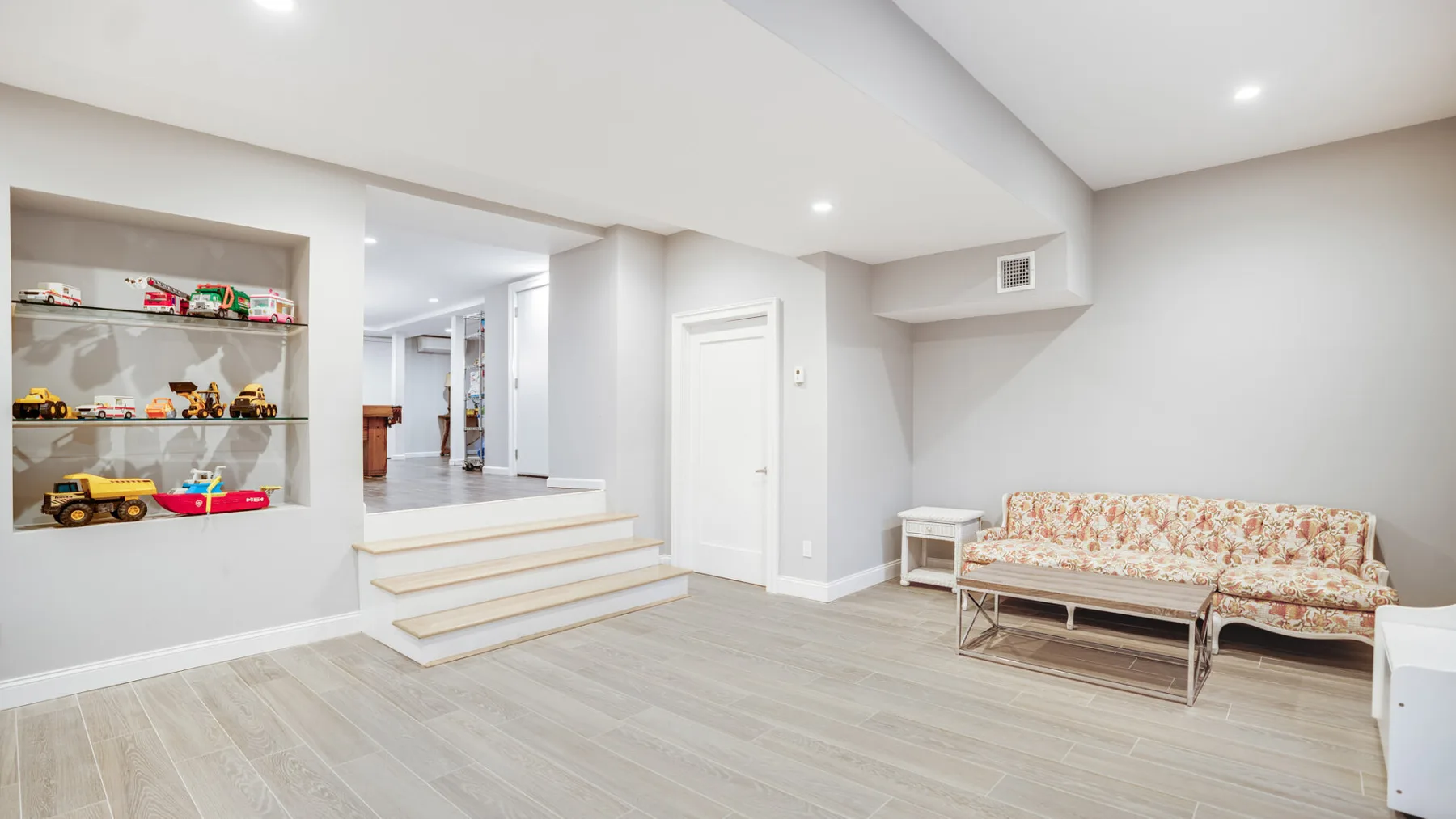 A bright basement lounge with built-in display shelves and a floral sofa.